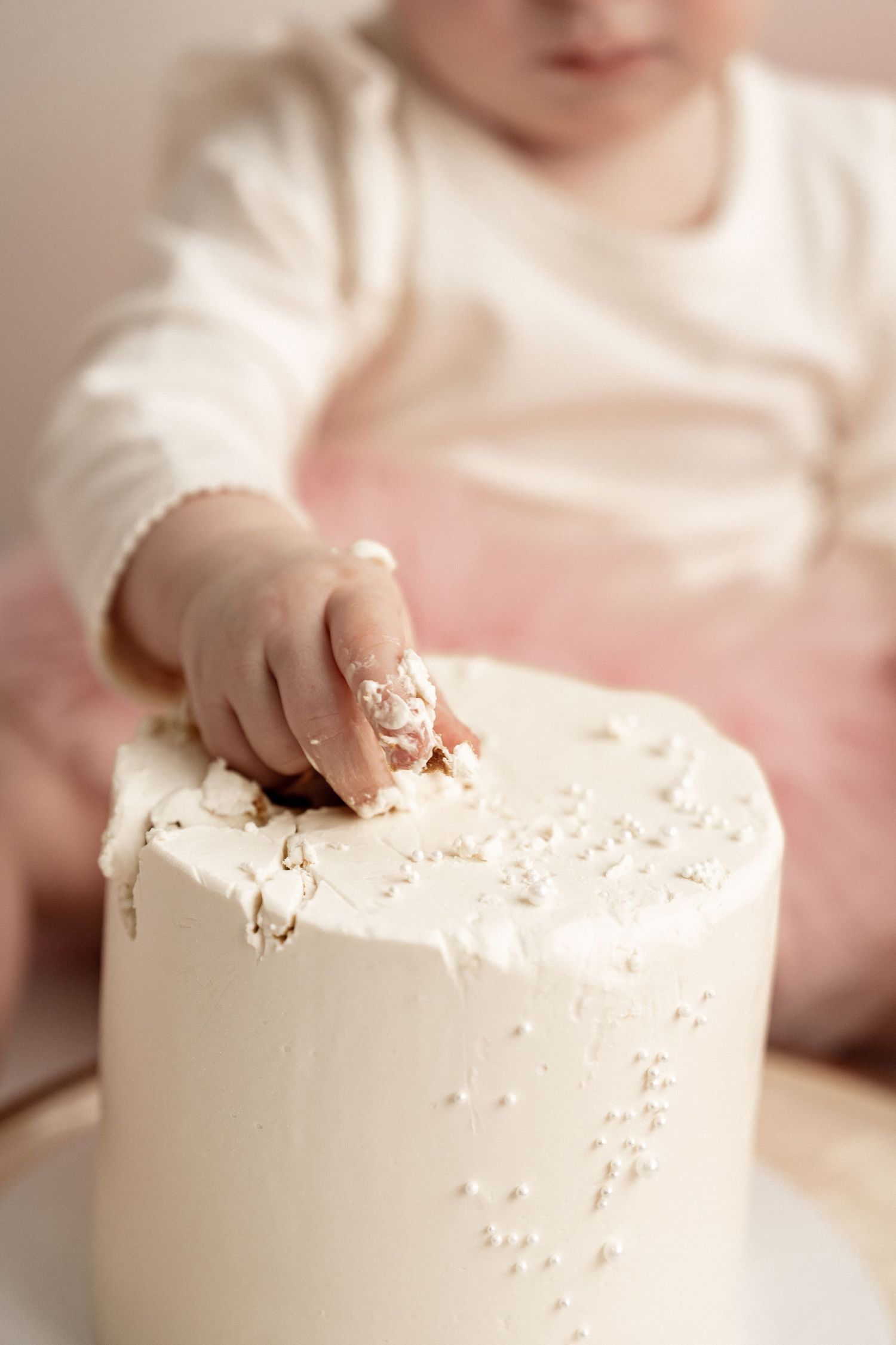 Small hands reaching to touch and explore a white frosted cake in a series of close-up shots.