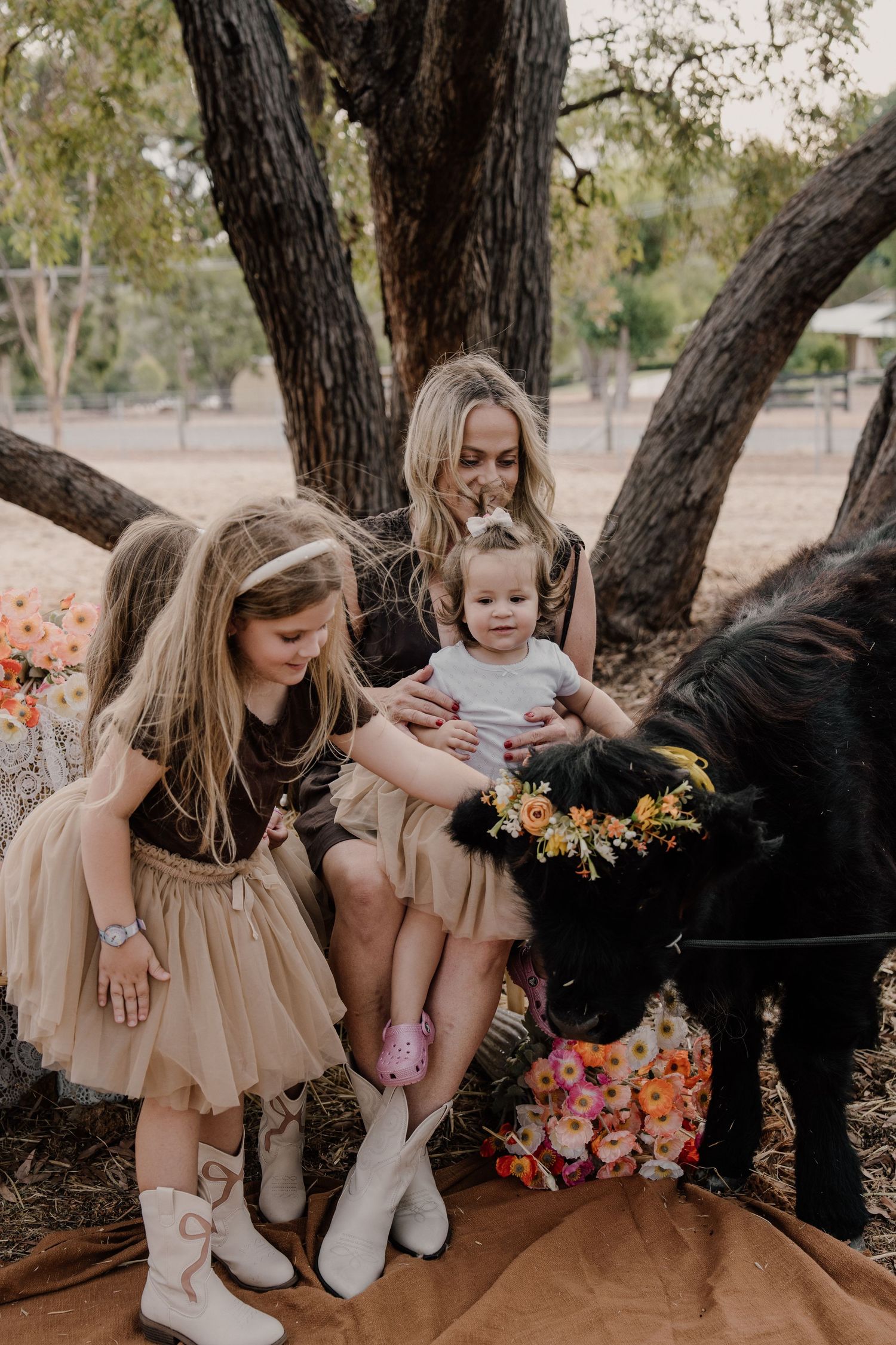 A series of rustic outdoor photos showing people in neutral dresses sitting on tree branches with floral arrangements.