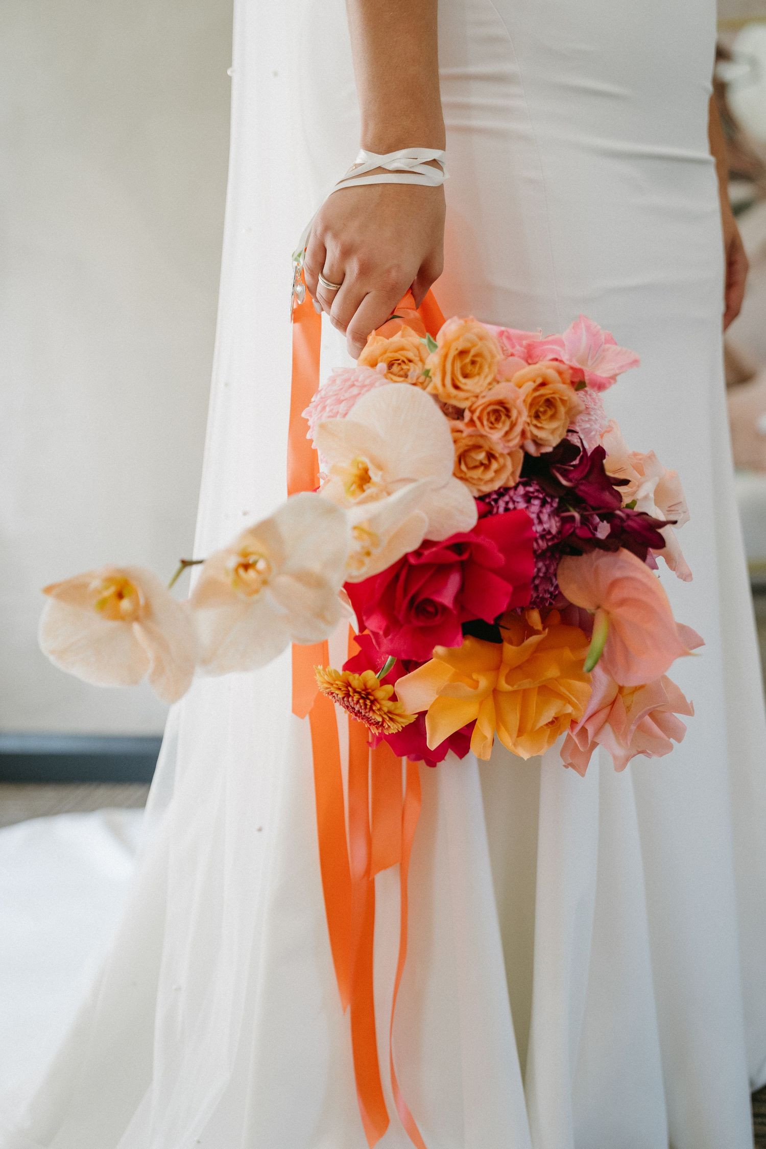 Elegant wedding bouquets featuring coral, burgundy and white flowers with peach orchids and orange ribbons against white dresses.