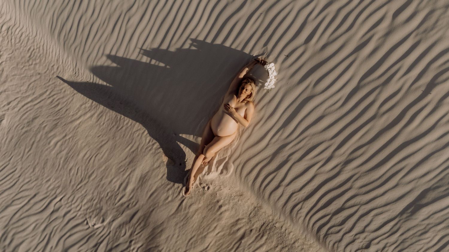 Artistic aerial view of person lying on rippled sand dunes creating dramatic shadows.