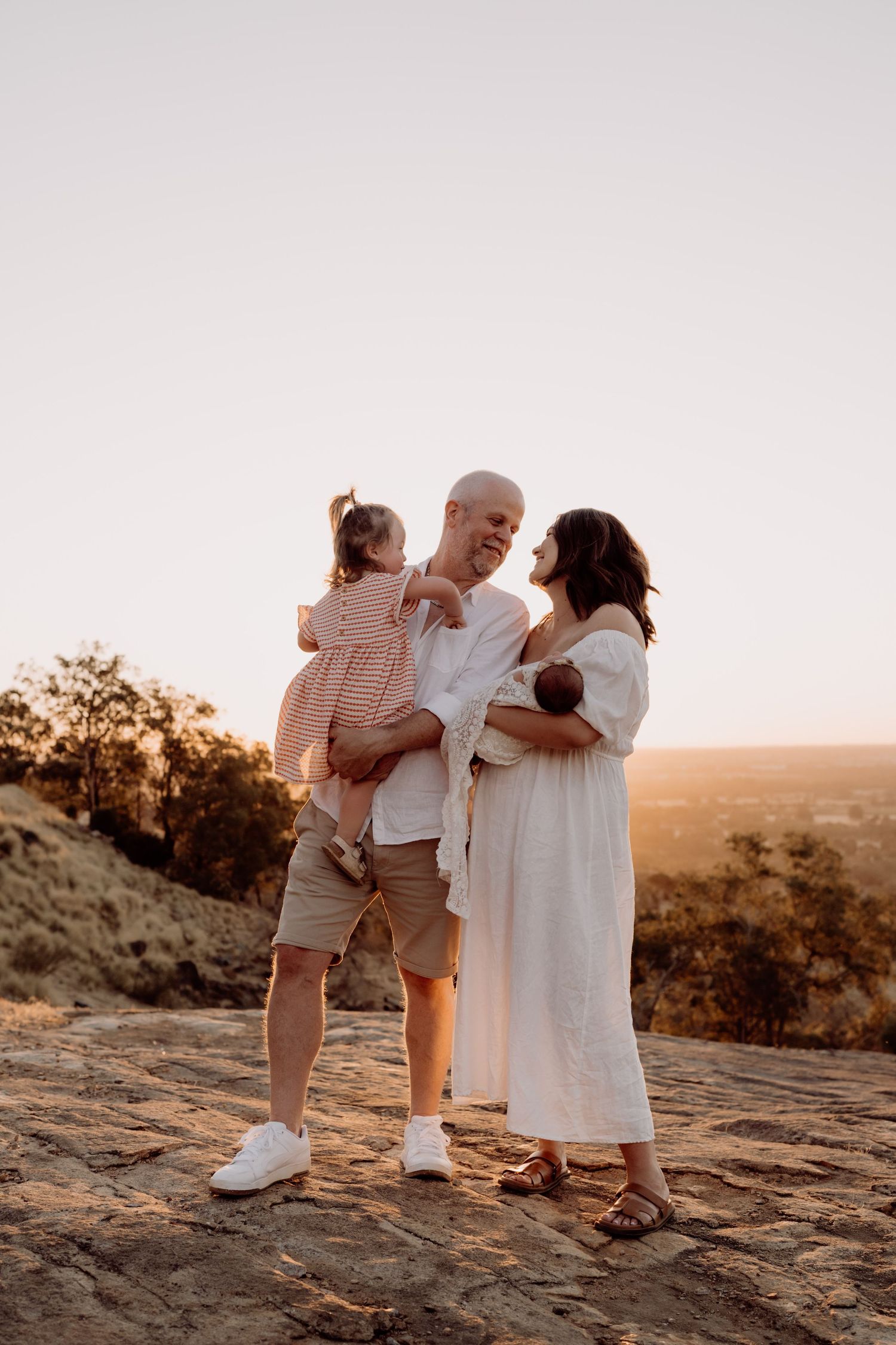 A family shares a tender moment together at sunset while standing on a rocky overlook in nature.