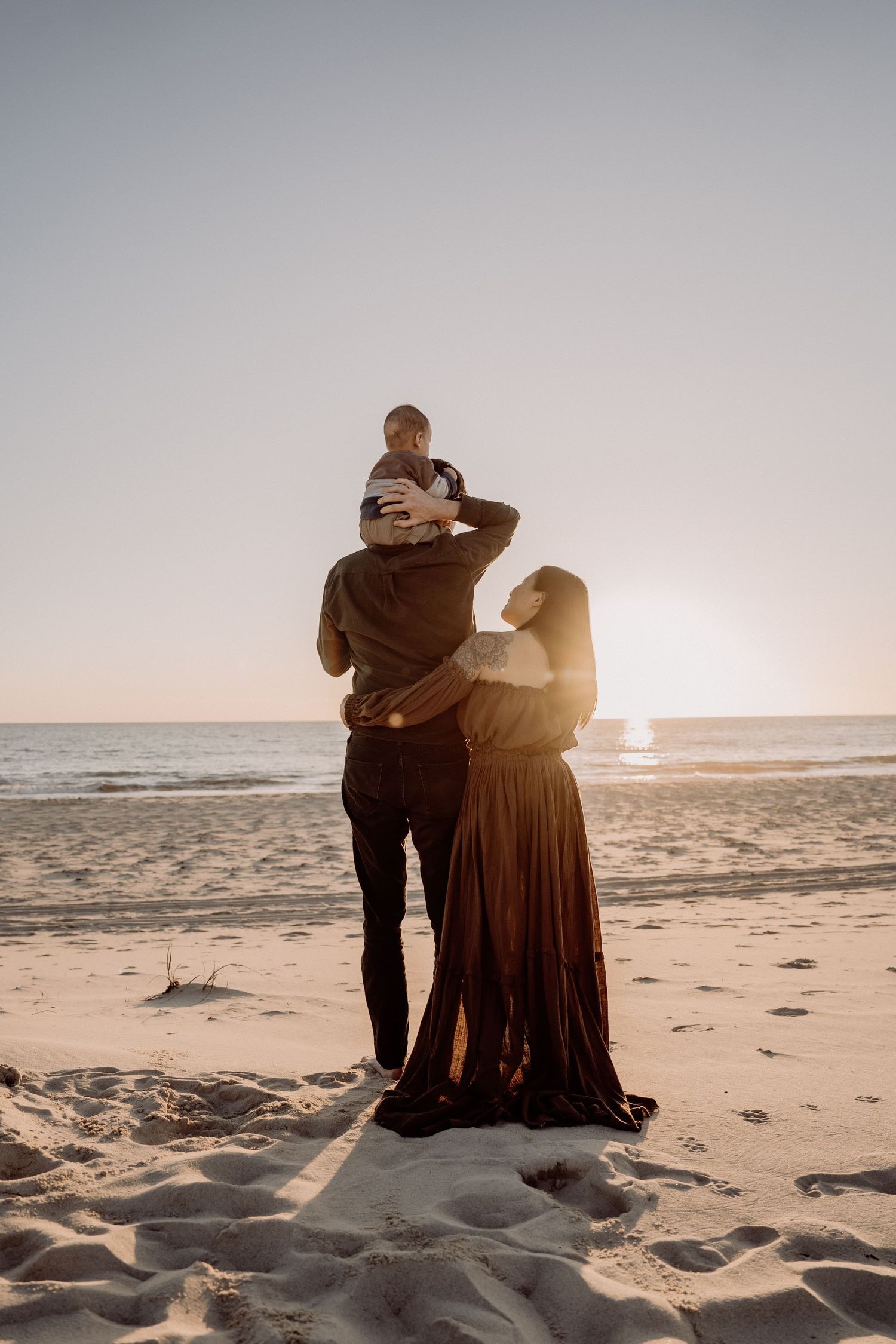 A couple sits close together on a sandy beach at sunset watching the ocean waves roll in peacefully.