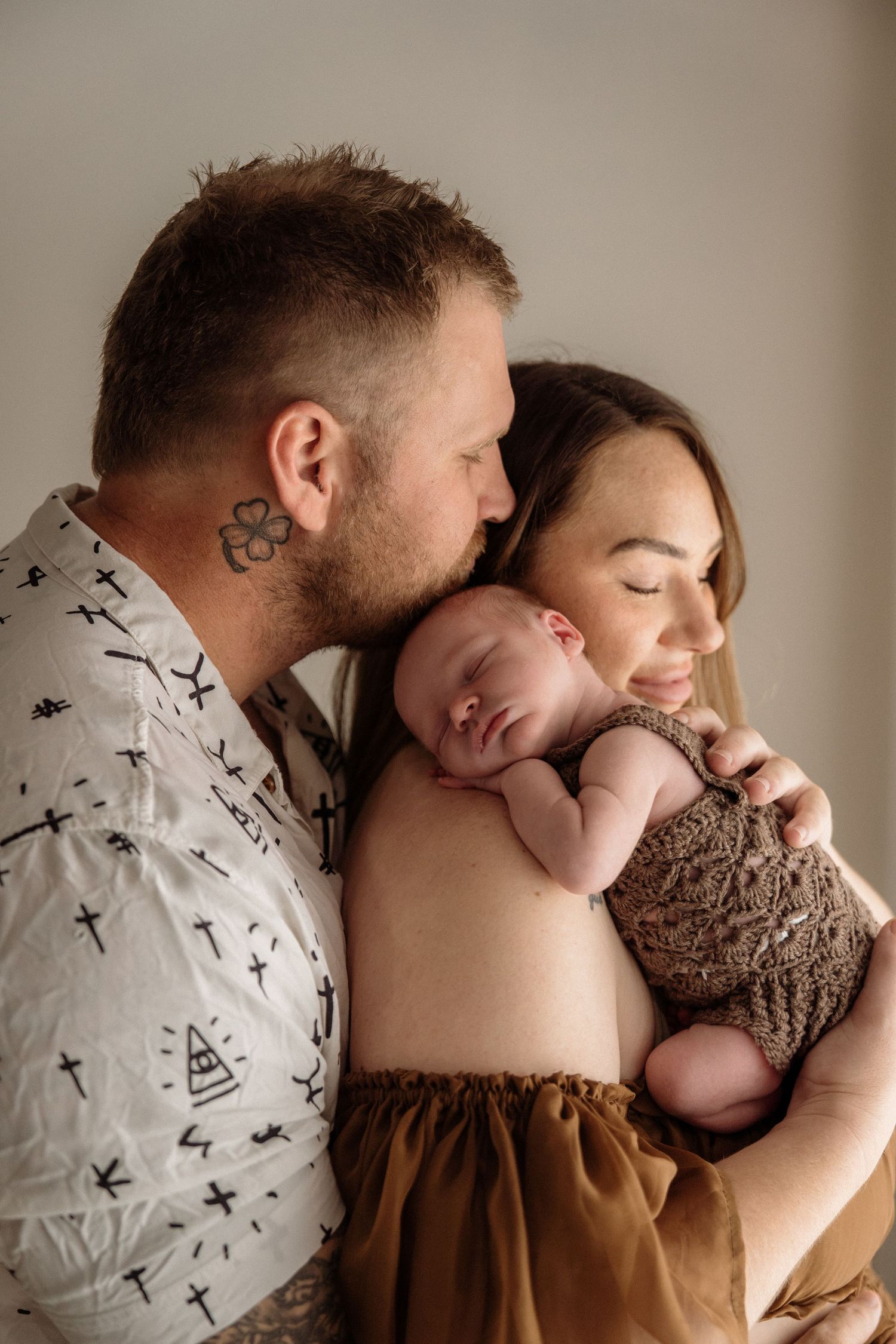 An intimate series showing tender moments between a couple holding their newborn baby wrapped in a brown blanket.