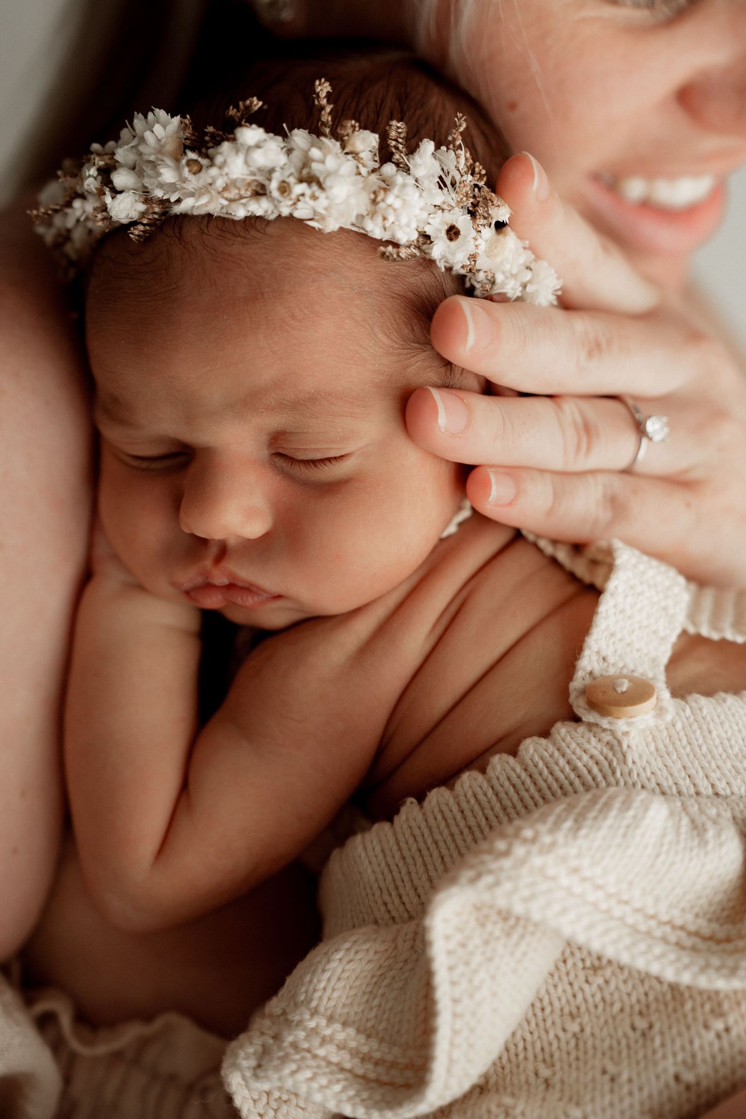 Peaceful sleeping newborn wearing delicate white floral crown and wrapped in soft knit blanket.