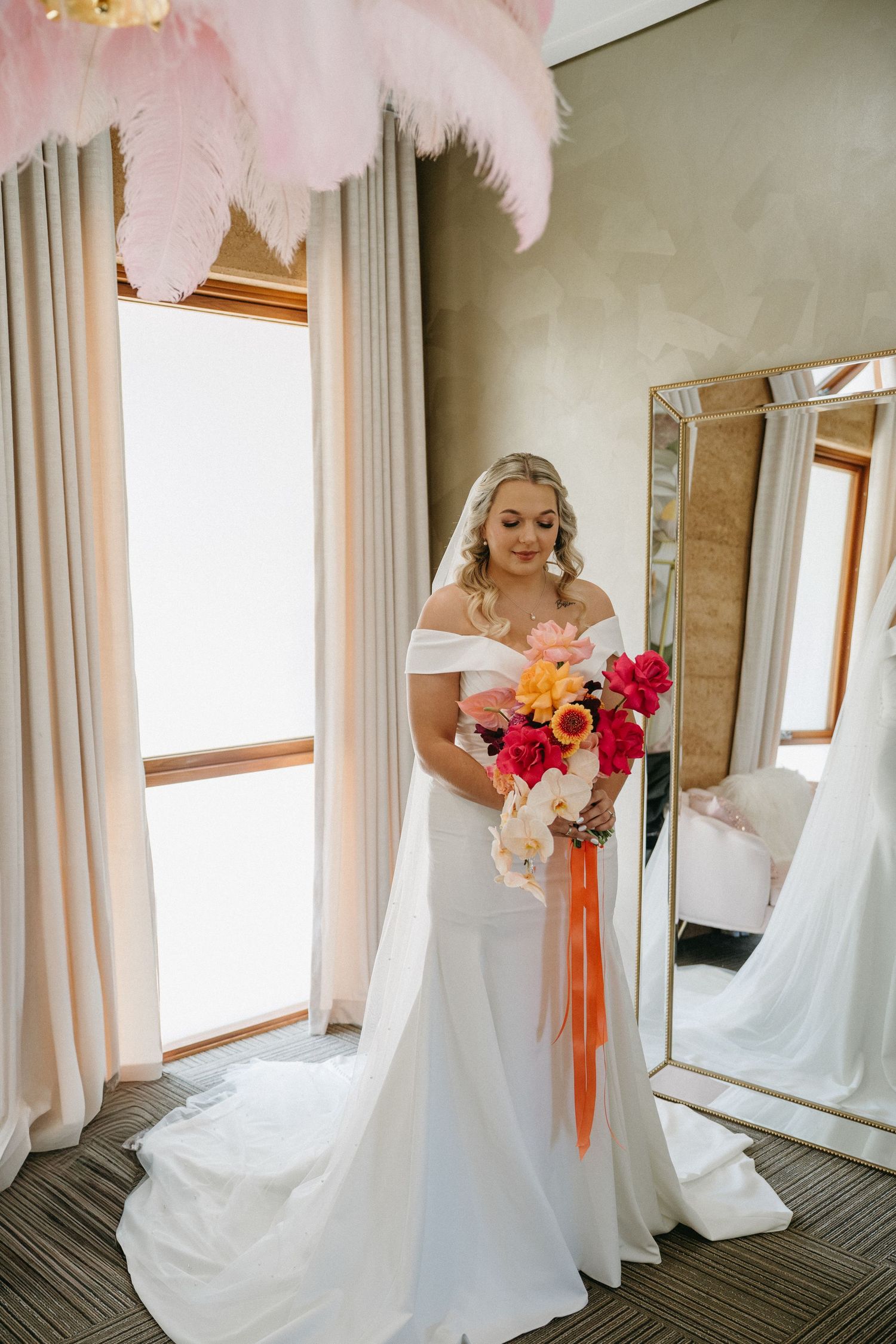 A bride in a white wedding dress holds a vibrant orange and pink floral bouquet while getting ready for her ceremony.