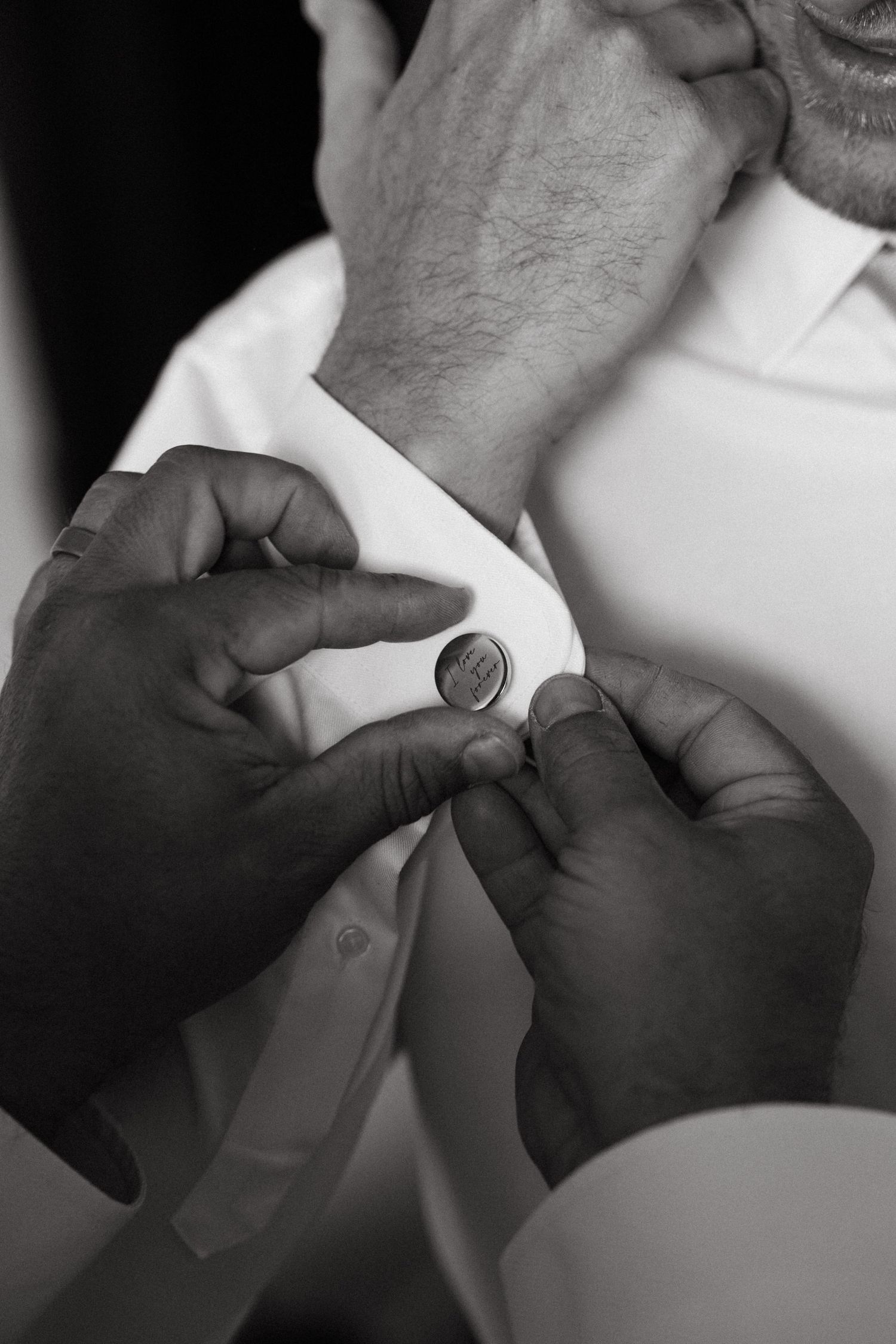 Close-up black and white photo of hands adjusting a cufflink on a formal white dress shirt.