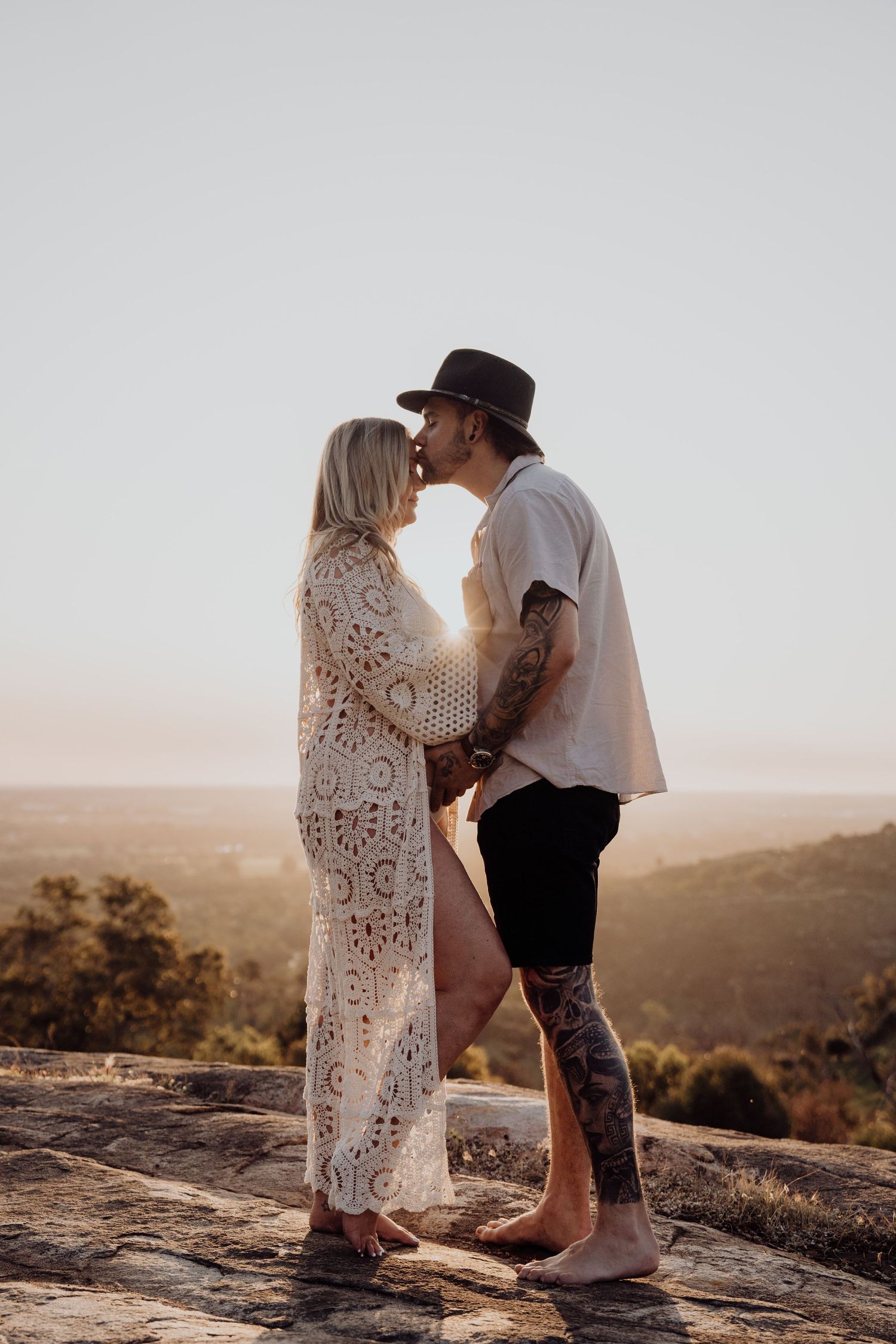 A couple holds each other tenderly while standing on a rocky overlook during sunset in a desert landscape.