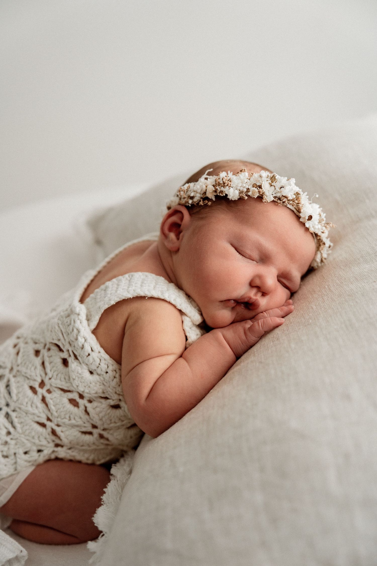 Sleeping newborn wearing delicate floral crown rests on white textured blanket in series of soft close-up shots.