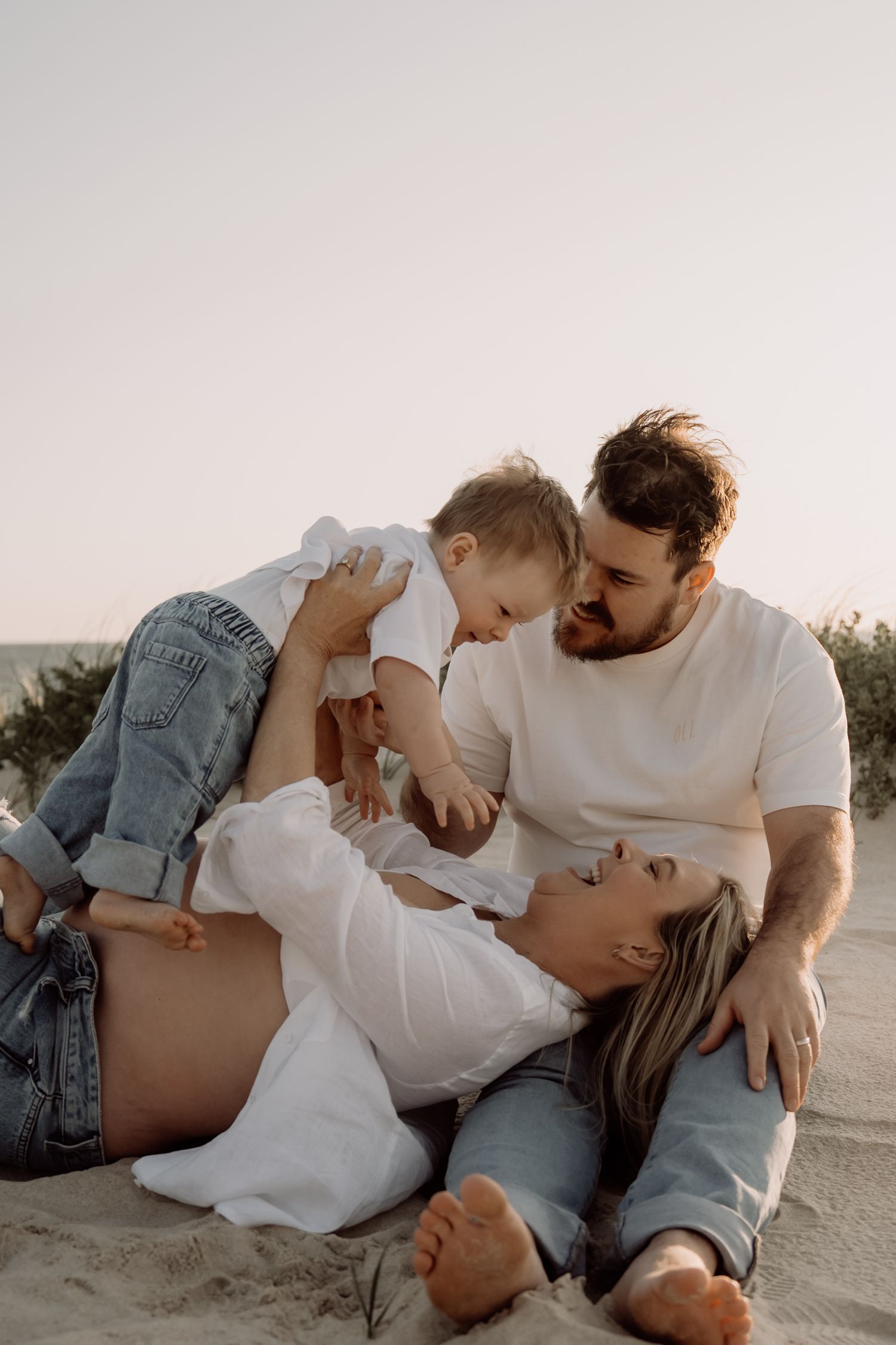 A family shares an intimate moment together lying on the beach at sunset.