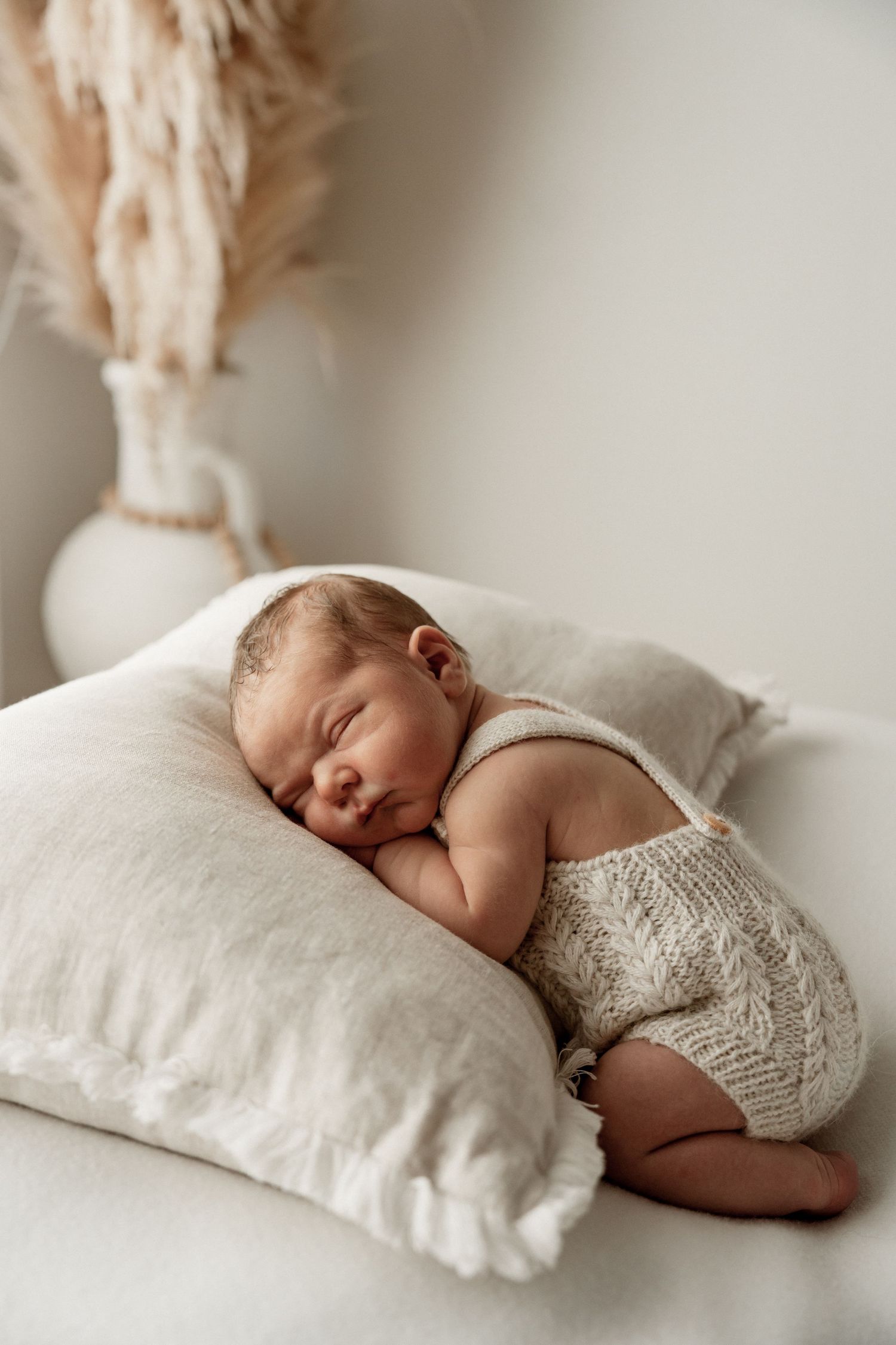 A sleeping newborn baby lies on soft white pillows wearing a delicate knit wrap in a series of peaceful poses.