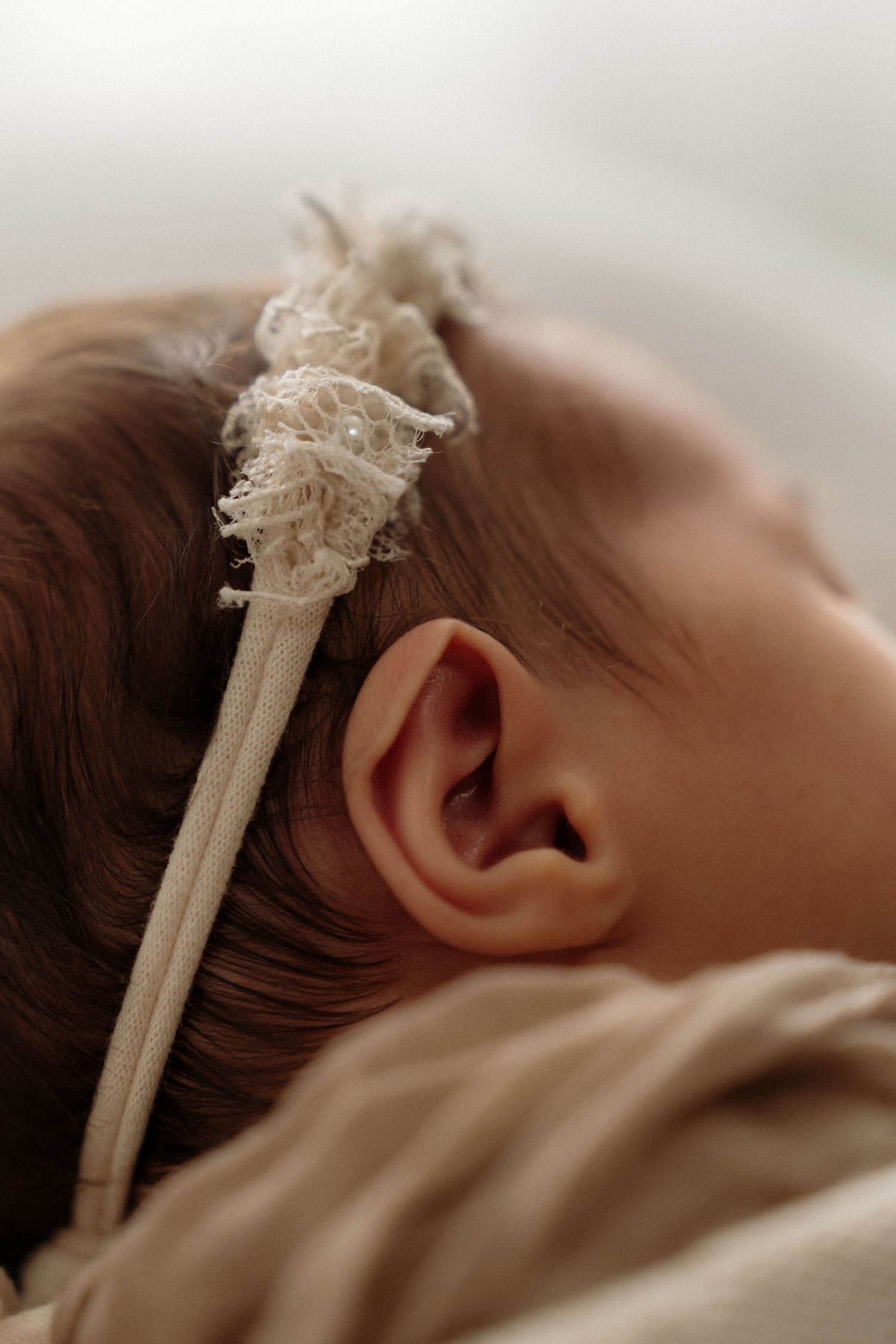 A close-up side view shows a white lace headband against brown hair in soft, muted lighting.
