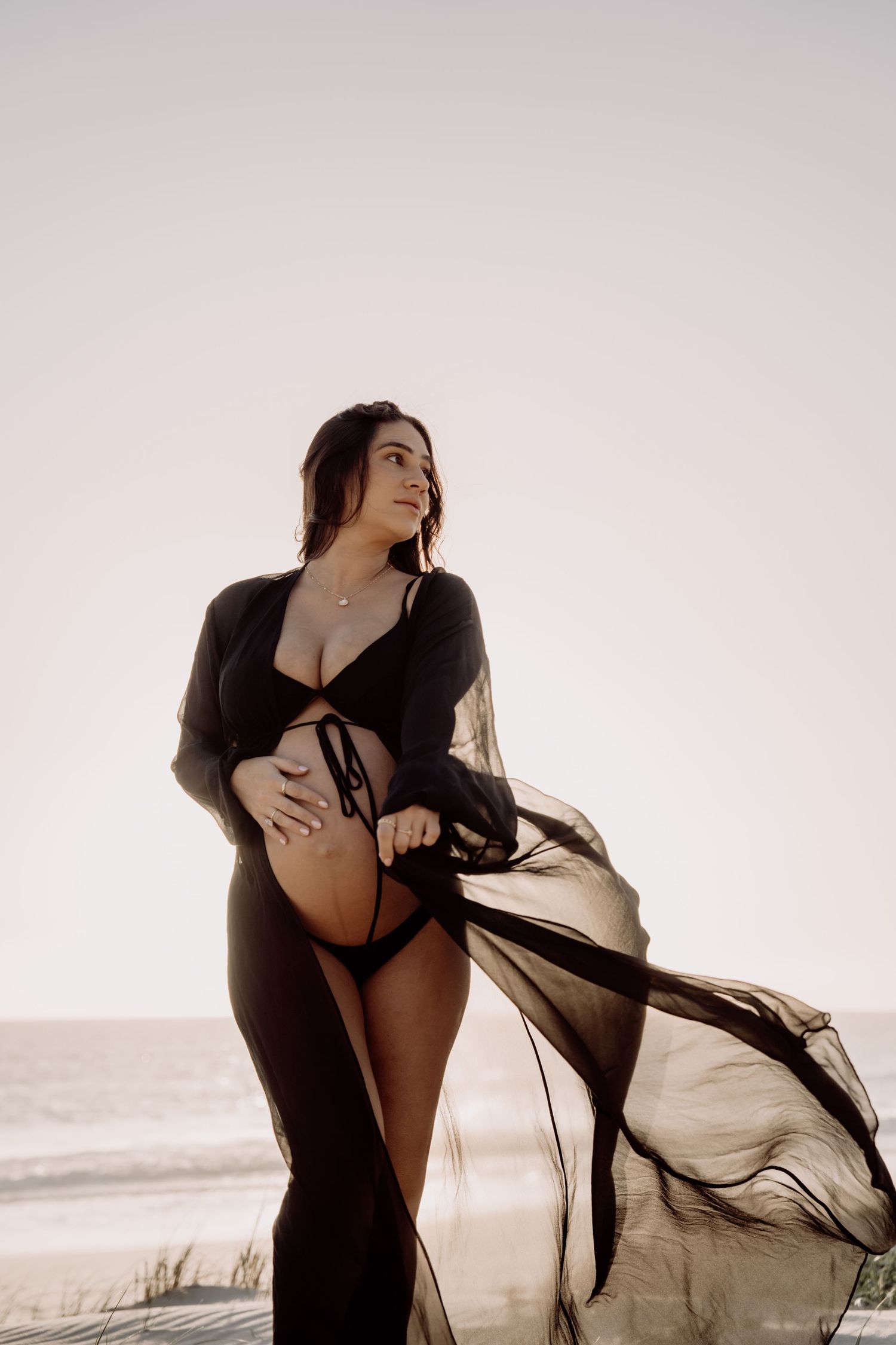 Artistic silhouette photos of person in flowy black fabric posed against misty beach backdrop at sunset.