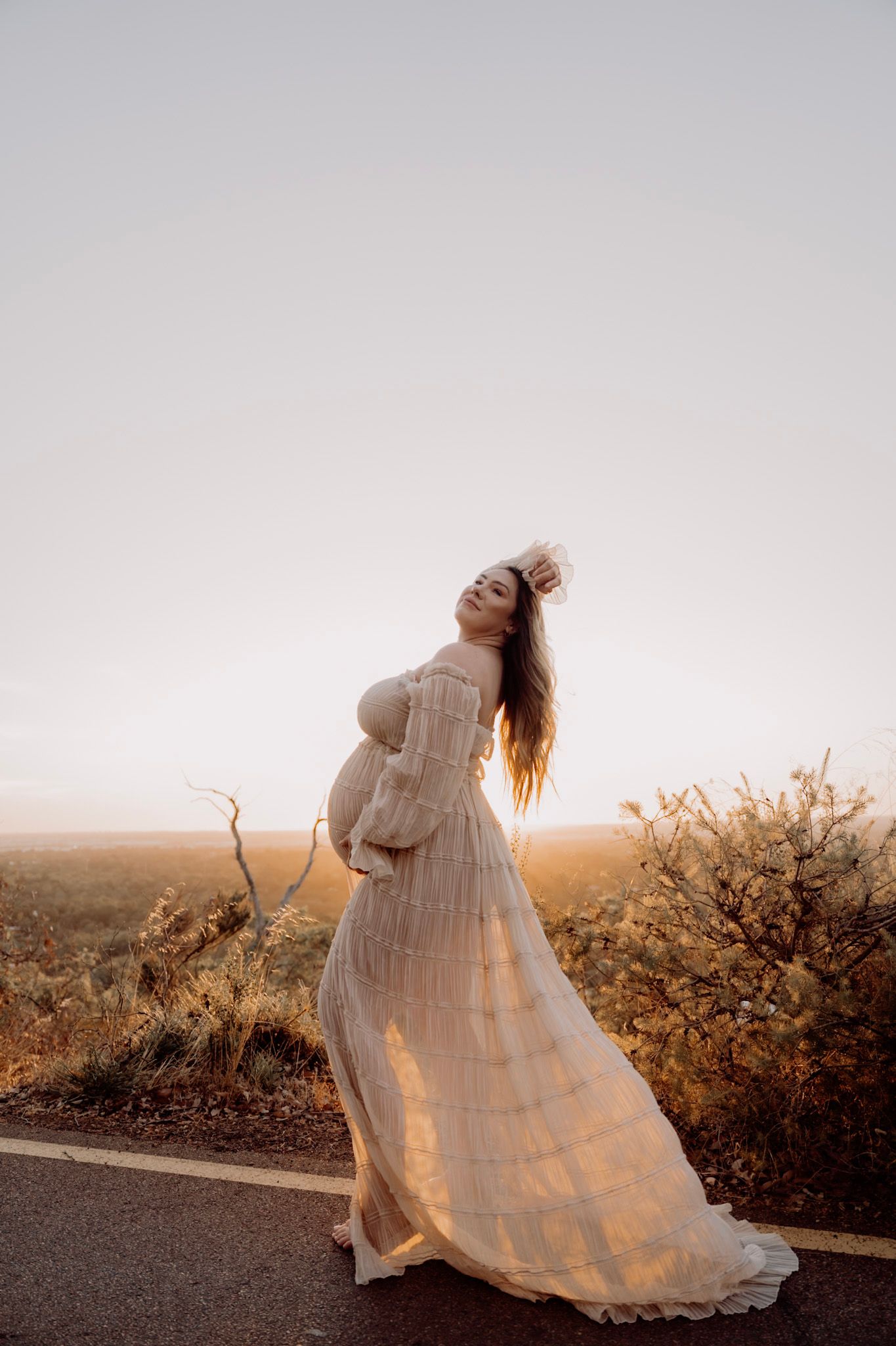 A person in a flowing white dress stands atop a hill at sunset, creating a dreamy ethereal silhouette against the horizon.