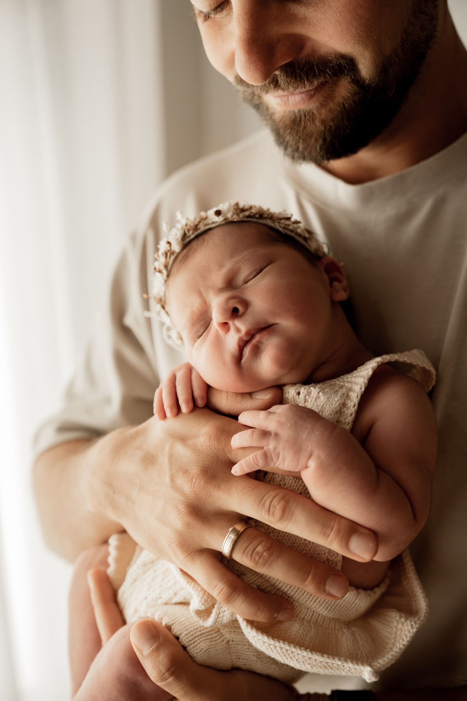 A series of tender moments showing hands cradling a sleeping newborn baby wrapped in a cream-colored blanket.