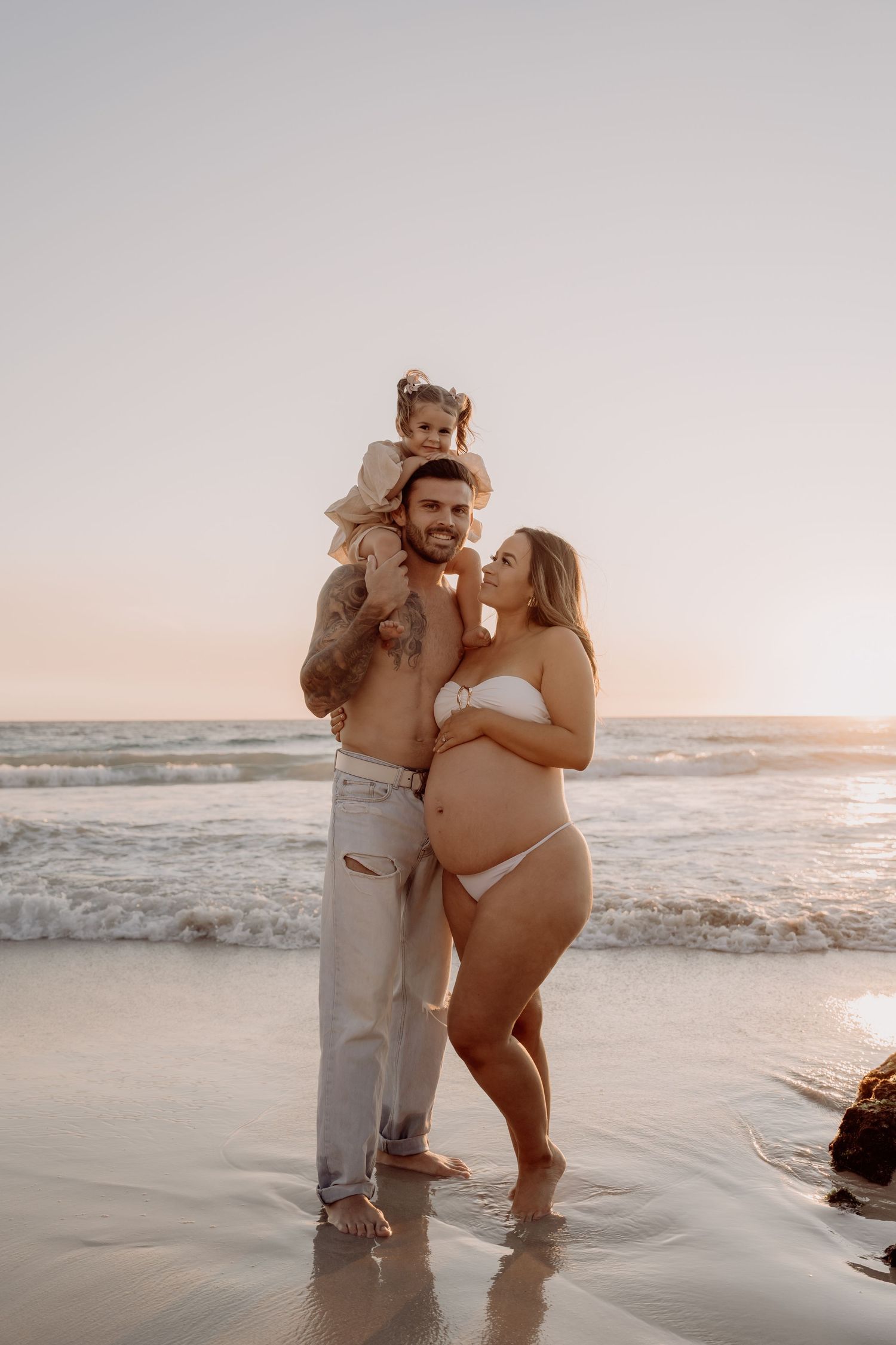 Family enjoying a sunset moment together on a beach with waves crashing in the background.