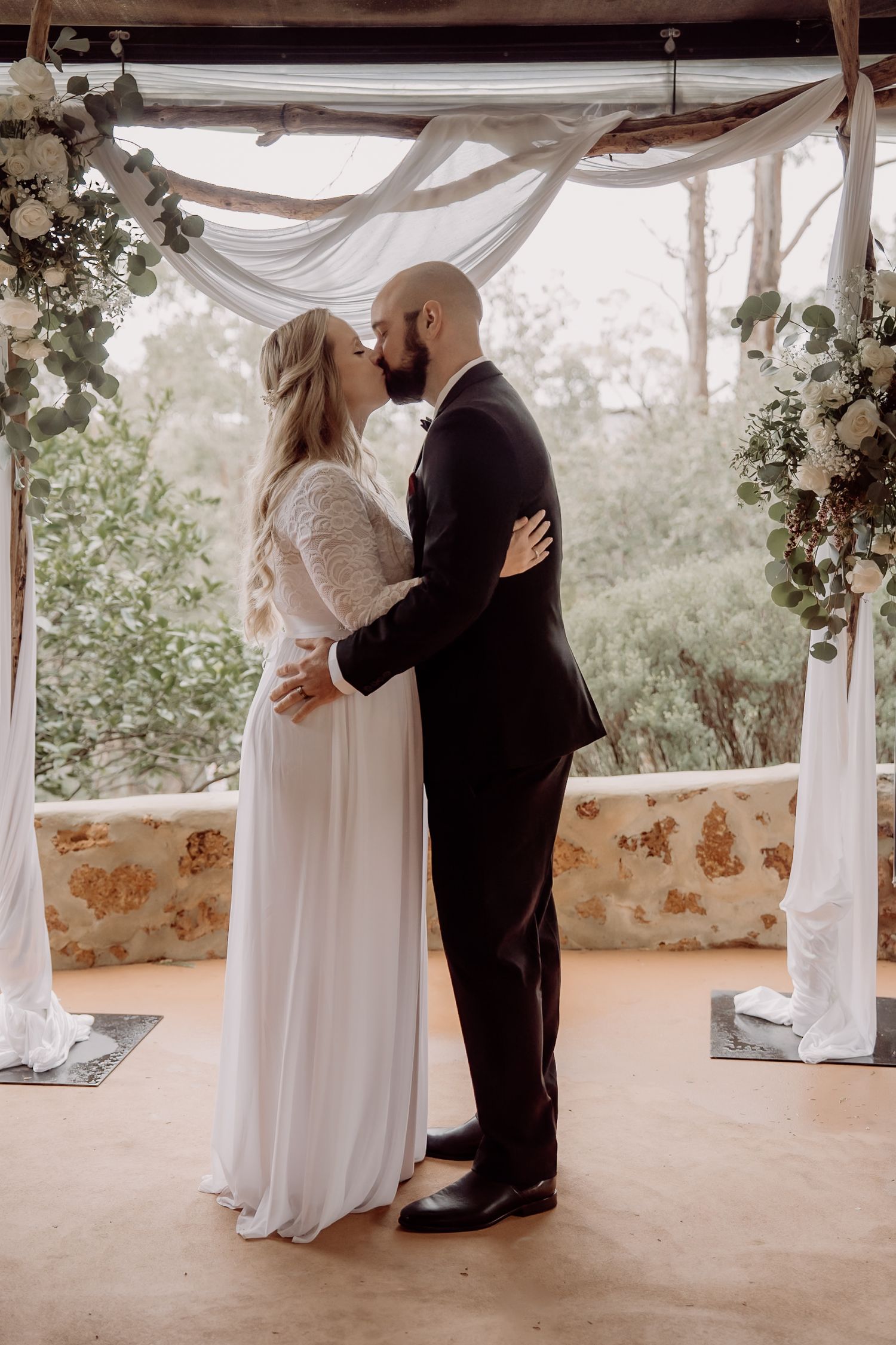 A romantic wedding ceremony under a draped canopy with white floral arrangements and soft lighting.