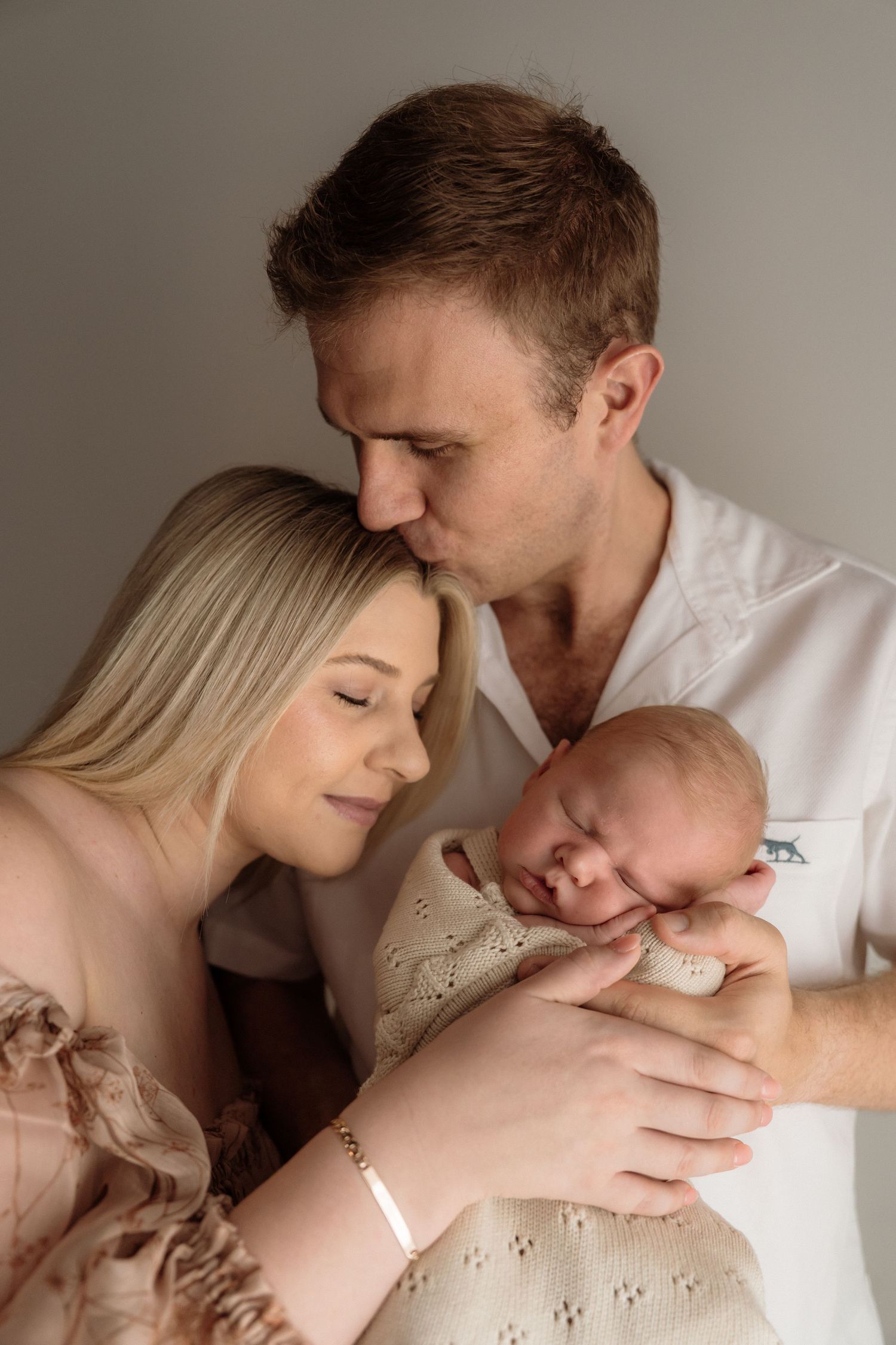 An intimate photo series showing a couple in soft light sharing tender moments and gentle kisses against a neutral background.