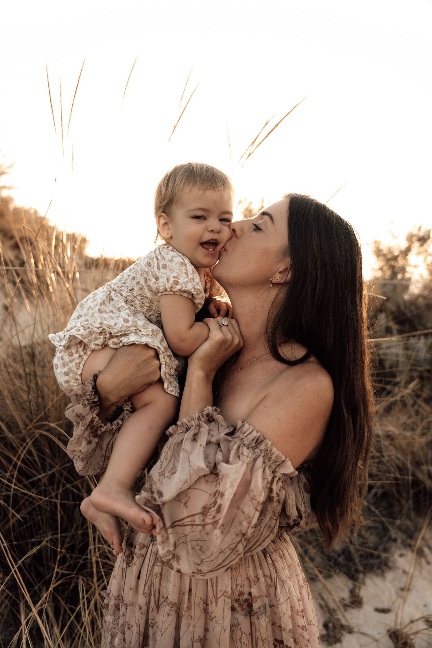 A tender moment captured between parent and child in a golden-lit field at sunset.