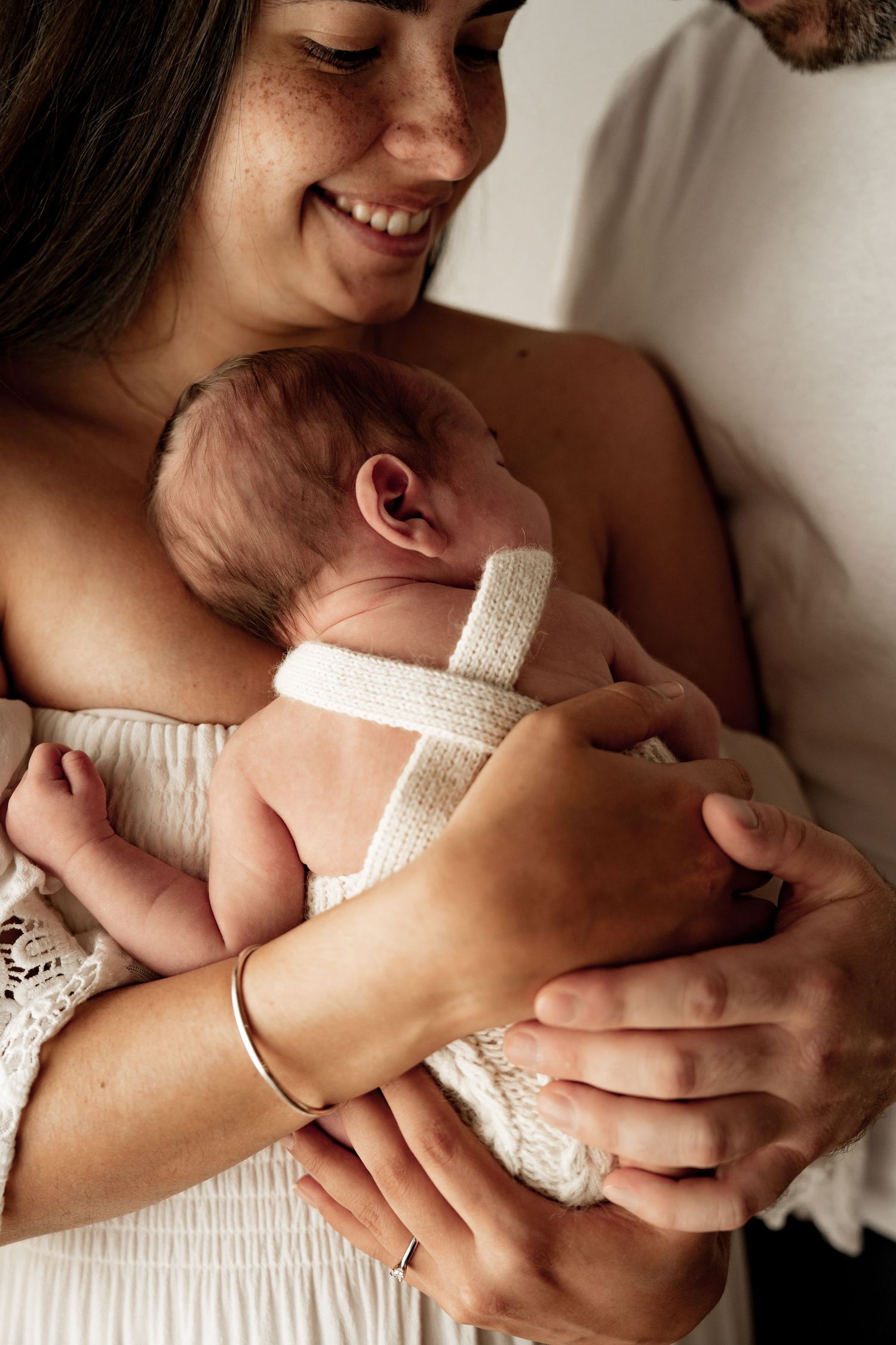 A series of tender moments showing a parent cradling a newborn baby in white clothing against a light background.