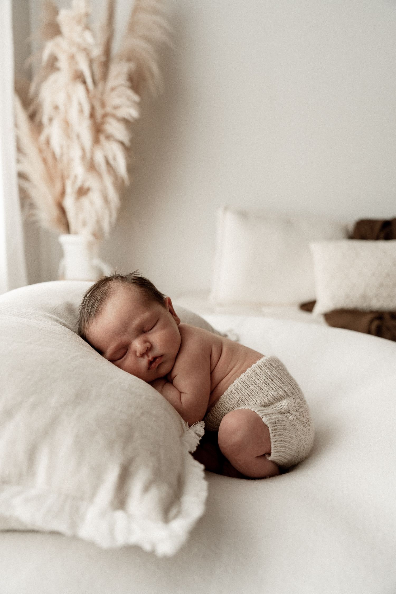 A peaceful newborn sleeping on soft white bedding in a minimalist setting with natural lighting.