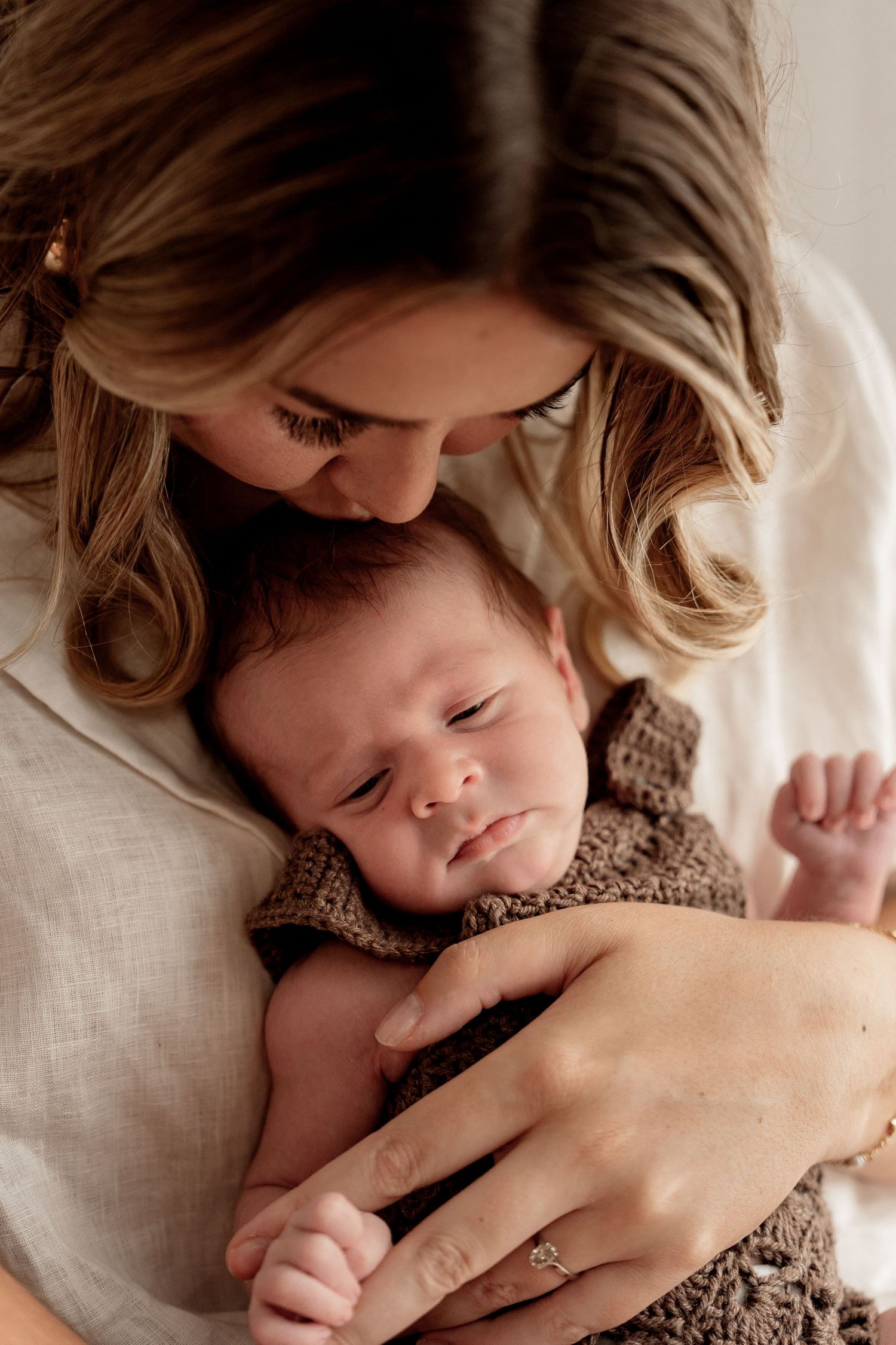Tender portrait of parent and infant laying together in serene embrace against soft white bedding.