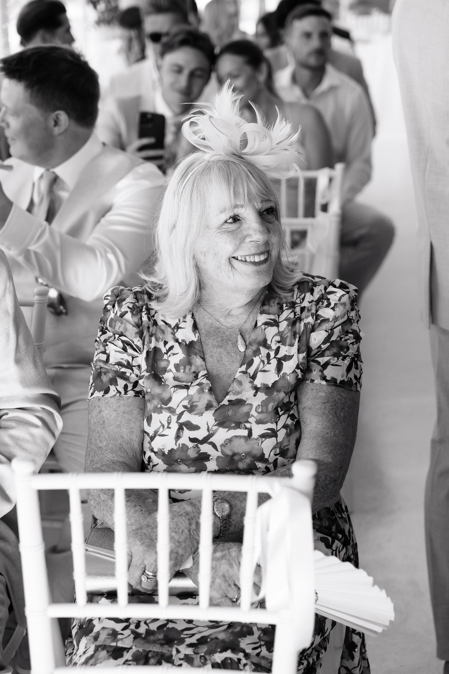 A candid black and white photo of a guest in a floral dress smiling during a wedding reception.