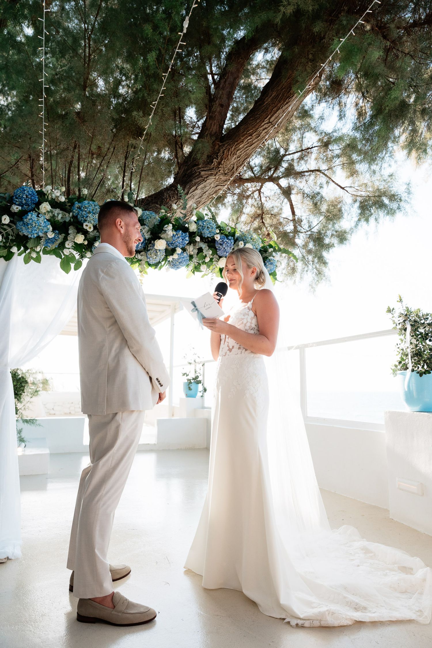 A romantic wedding photo sequence showing a couple in white attire sharing a first look moment under trees with blue decor.