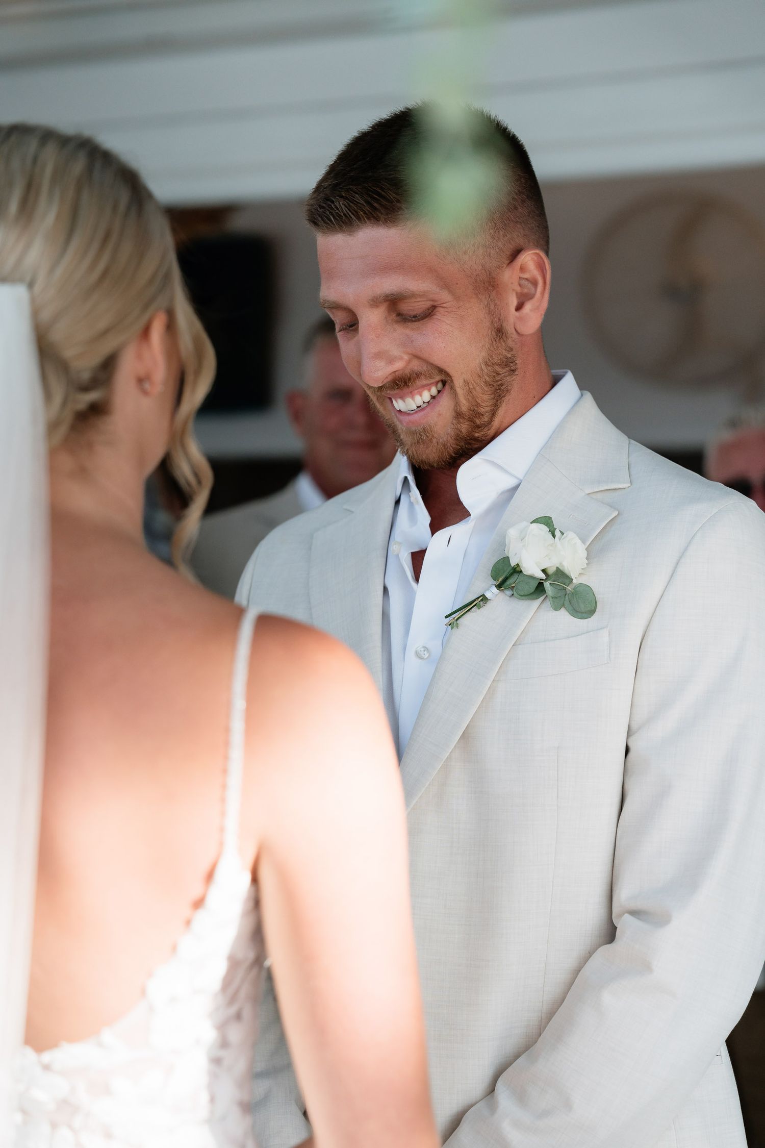 A couple shares an intimate moment in white wedding attire with delicate floral boutonnieres.