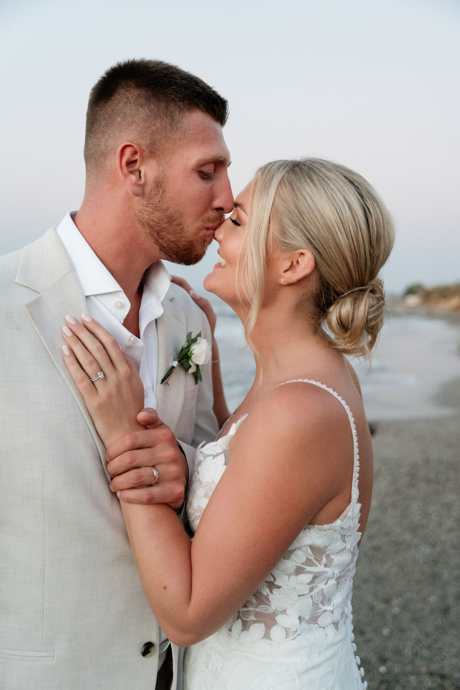 Romantic couple shares intimate moments on a beach at sunset in elegant wedding attire.