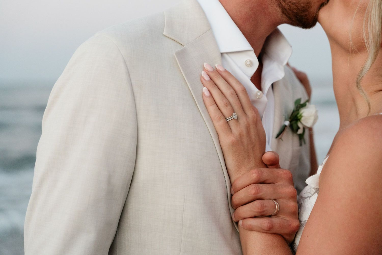A romantic couple in light colored wedding attire share intimate moments during a beach photo session at sunset.