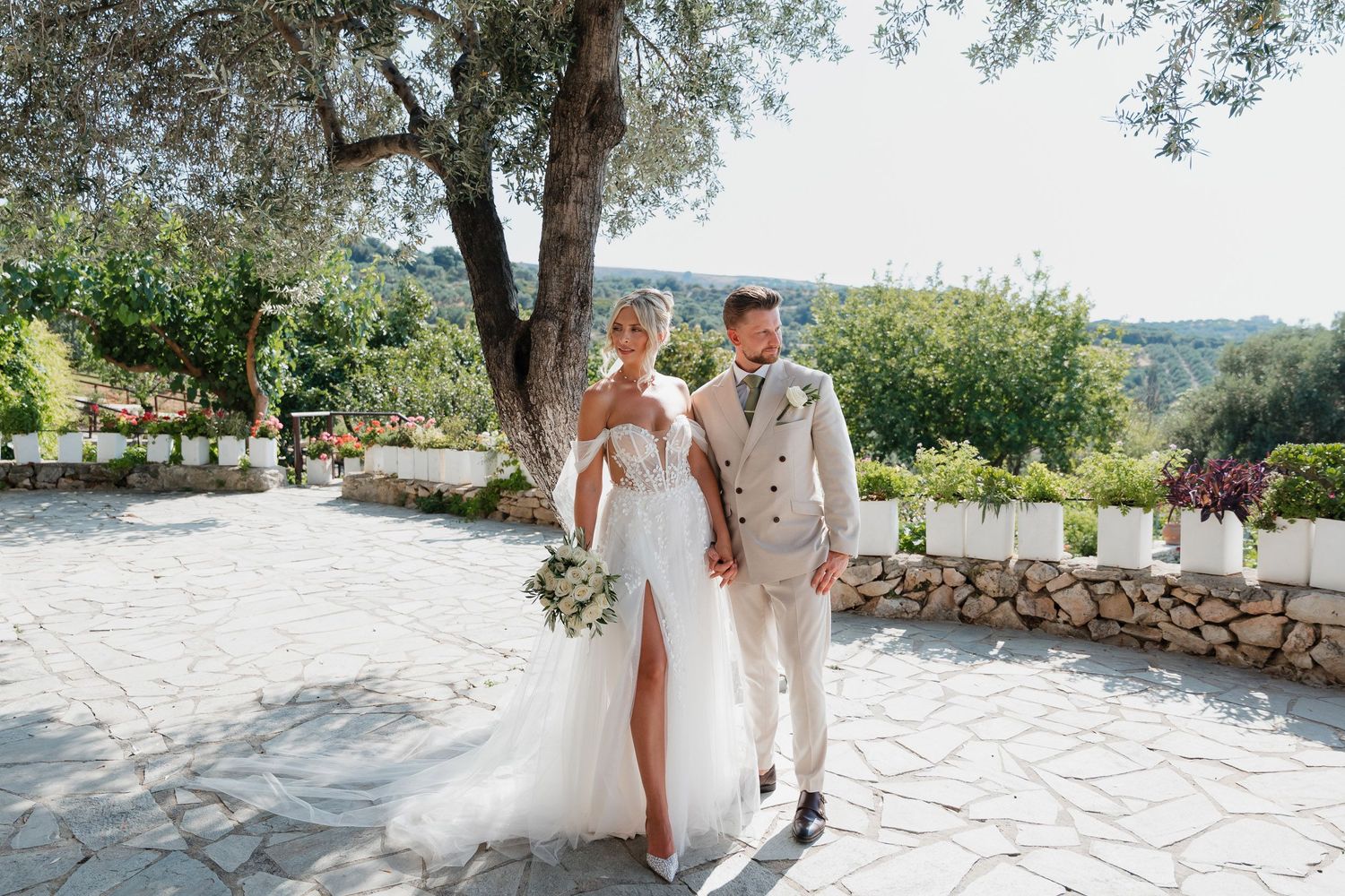 A romantic outdoor wedding ceremony in a Mediterranean setting with olive trees and stone pathways.