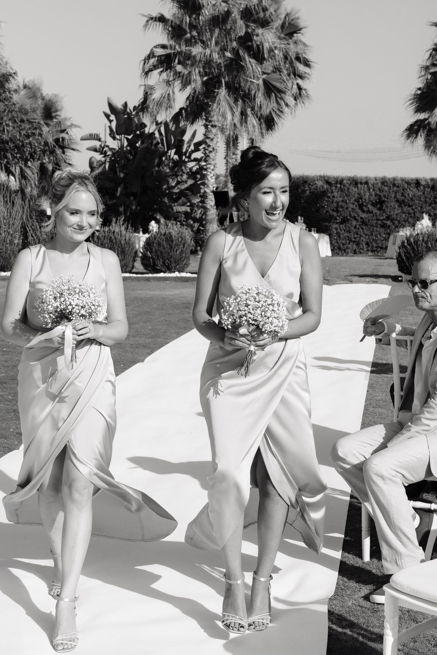 A sequence of black and white photos showing a group of people in white outfits dancing outdoors with palm trees in the background.