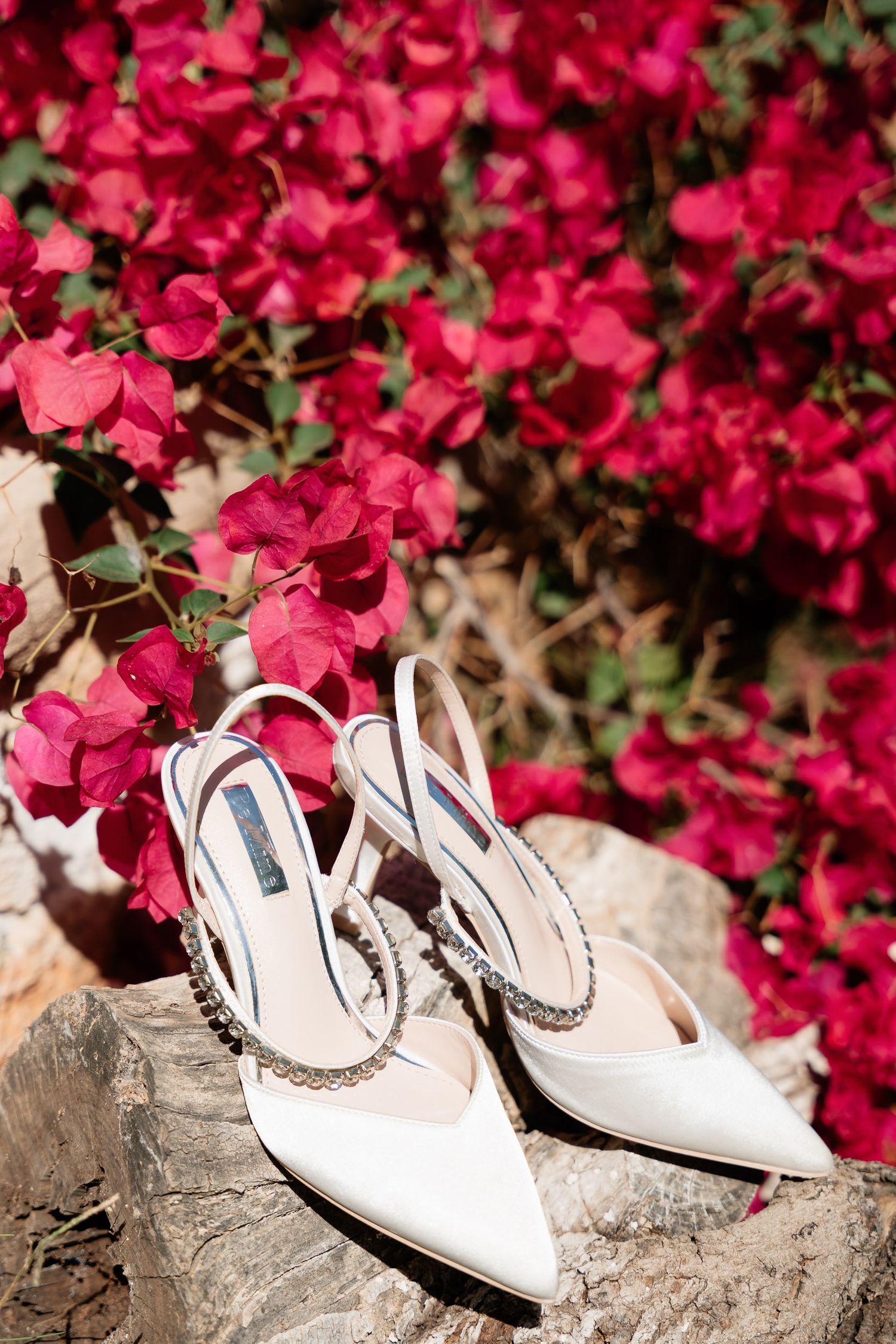 White bridal shoes arranged on stone steps with vibrant pink flowers creating a romantic backdrop.