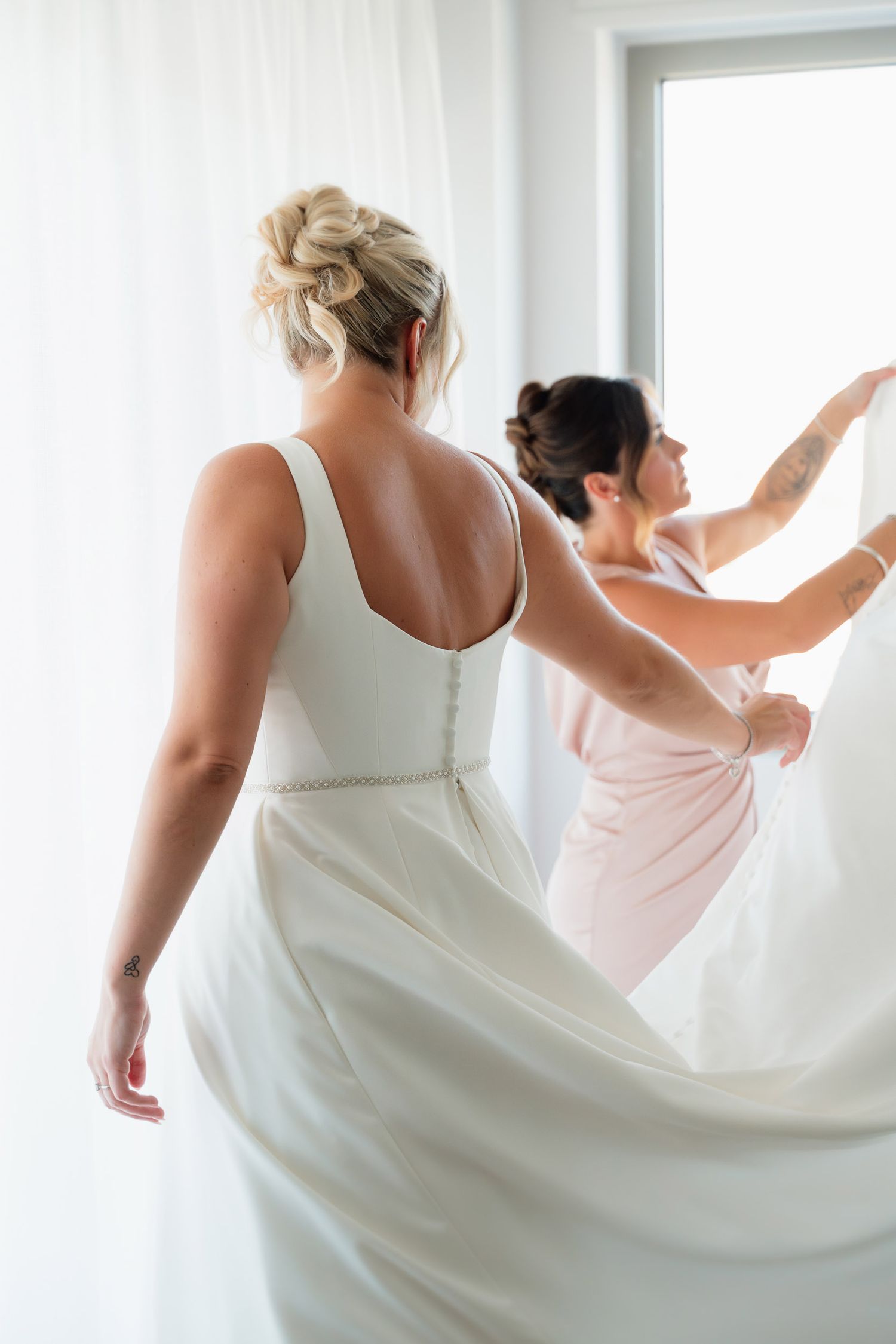Two dancers in flowing white dresses practicing graceful movements by a bright window.