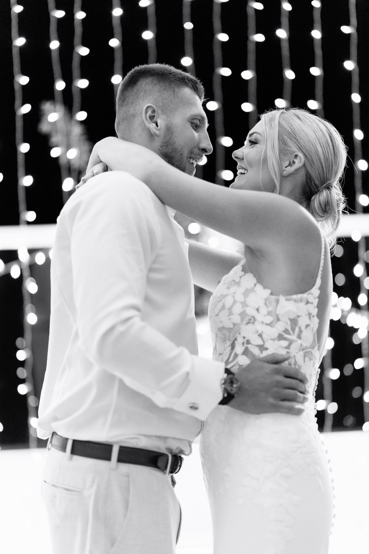 A romantic wedding couple shares their first dance under twinkling string lights at an elegant reception.