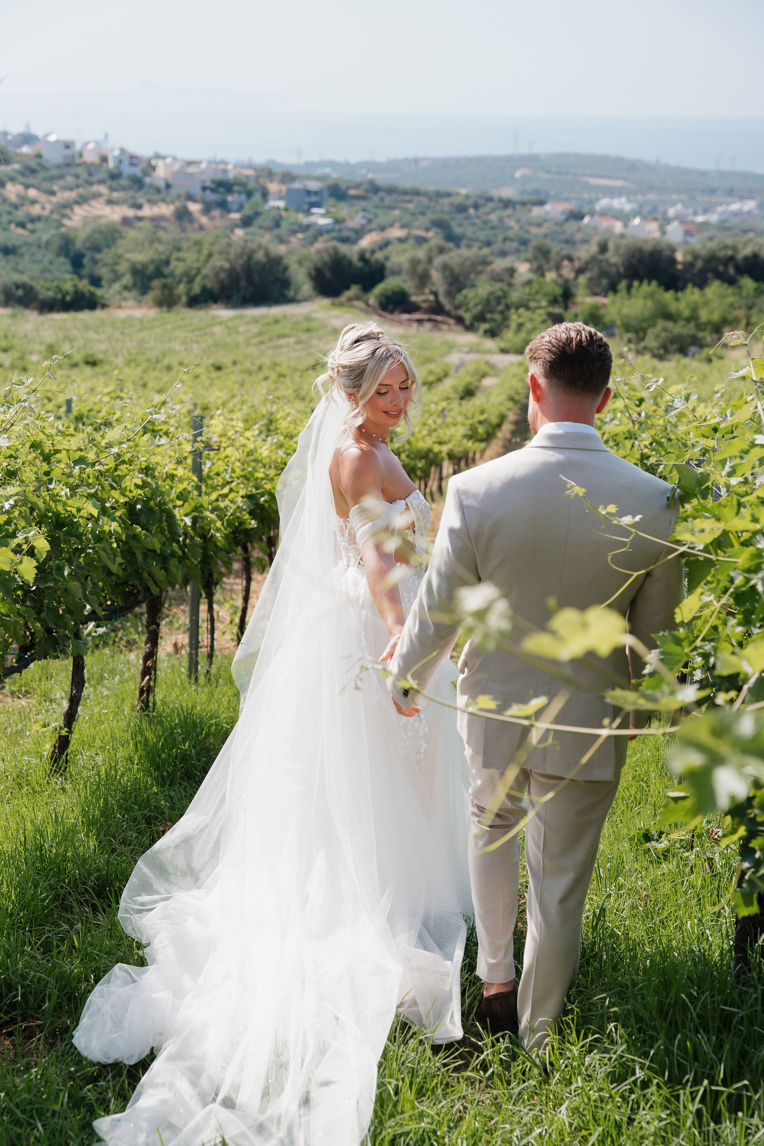 A couple shares a romantic moment among lush green vineyard rows with rolling hills and countryside in the background.