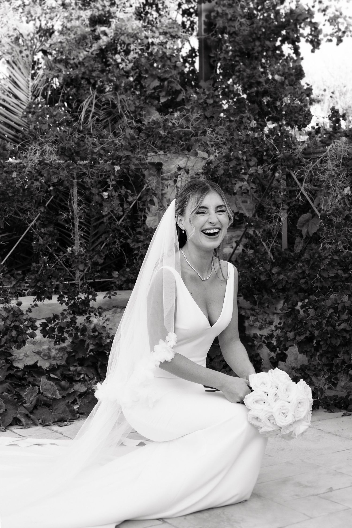 A bride in a flowing white wedding dress poses playfully in a series of black and white photos outdoors.