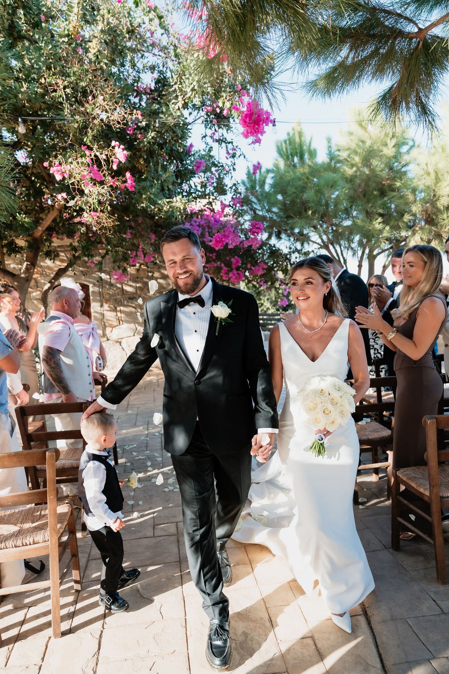 A wedding celebration at an outdoor venue with beautiful pink bougainvillea flowers and natural sunlight streaming through the trees.