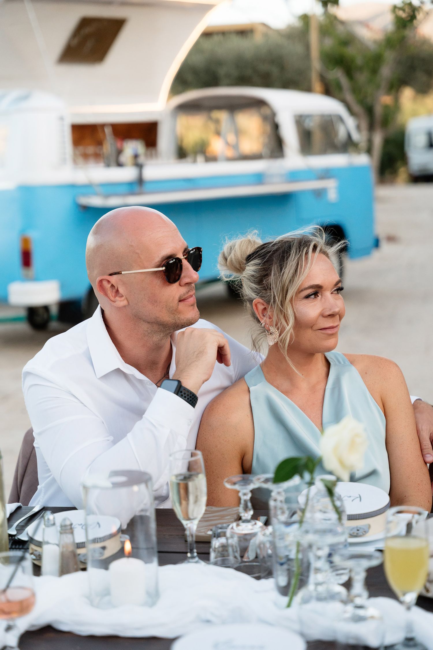 Couple dining outdoors at elegant table setting with vintage blue food truck in background.