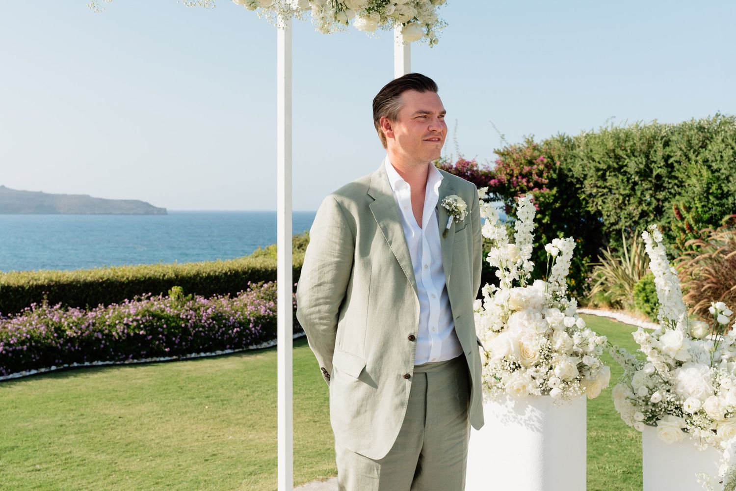 Elegant outdoor wedding ceremony setup with white floral arrangements and ocean view backdrop on a sunny day.