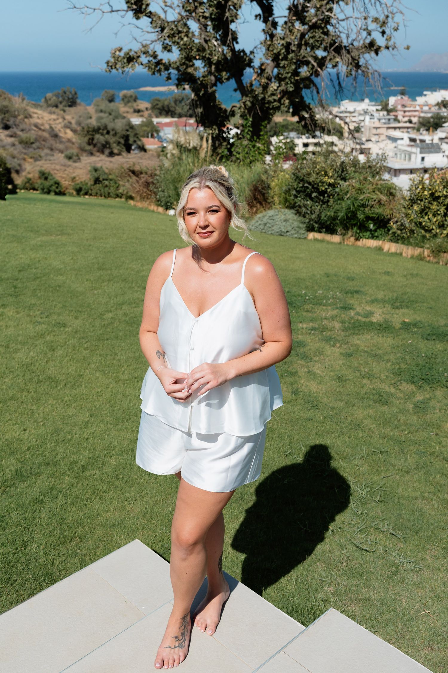 A white summer outfit on a grassy hilltop overlooking coastal buildings and ocean views on a sunny day.