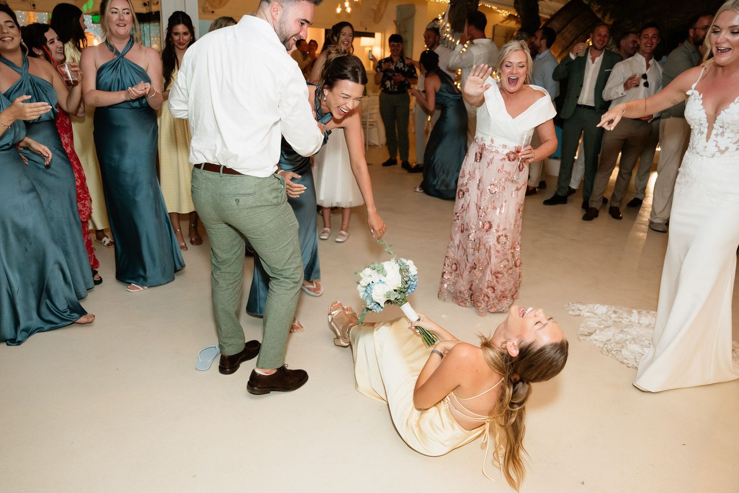 A group of wedding guests dance and celebrate together on a dance floor during a reception party.
