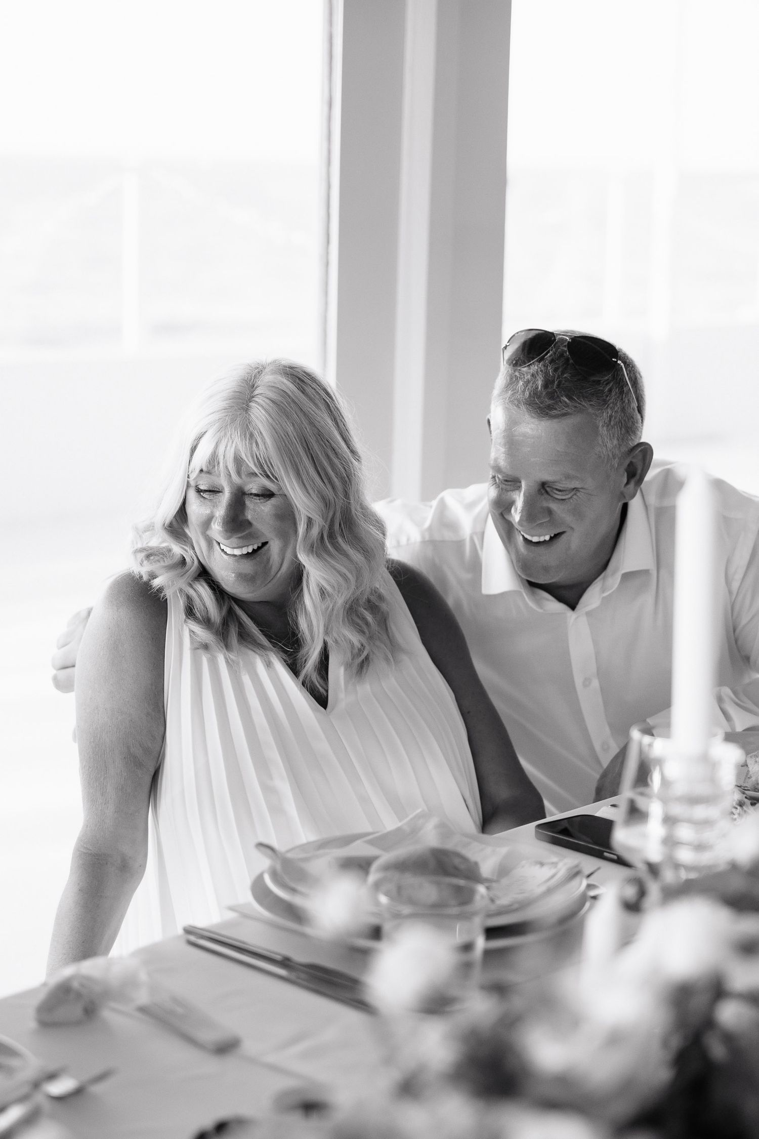 A couple shares a joyful moment while dining together at a bright indoor setting, captured in black and white.