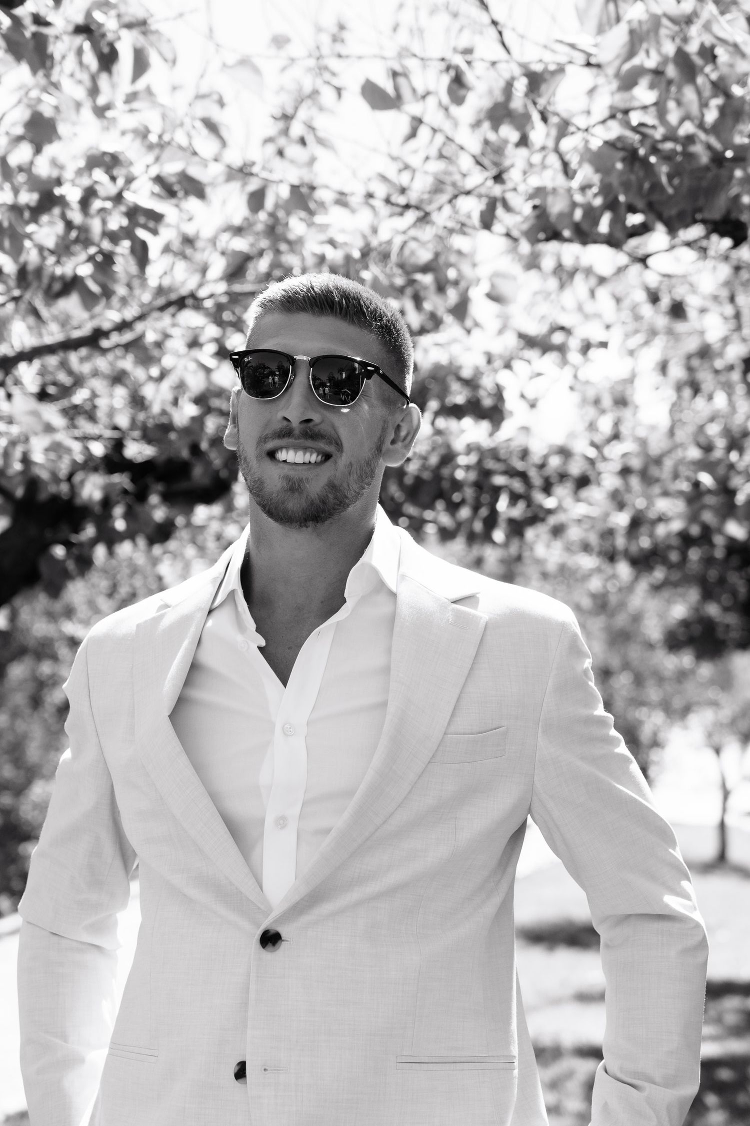 Four black and white photos showing a person in a white suit jacket posing outdoors on a sunny day.