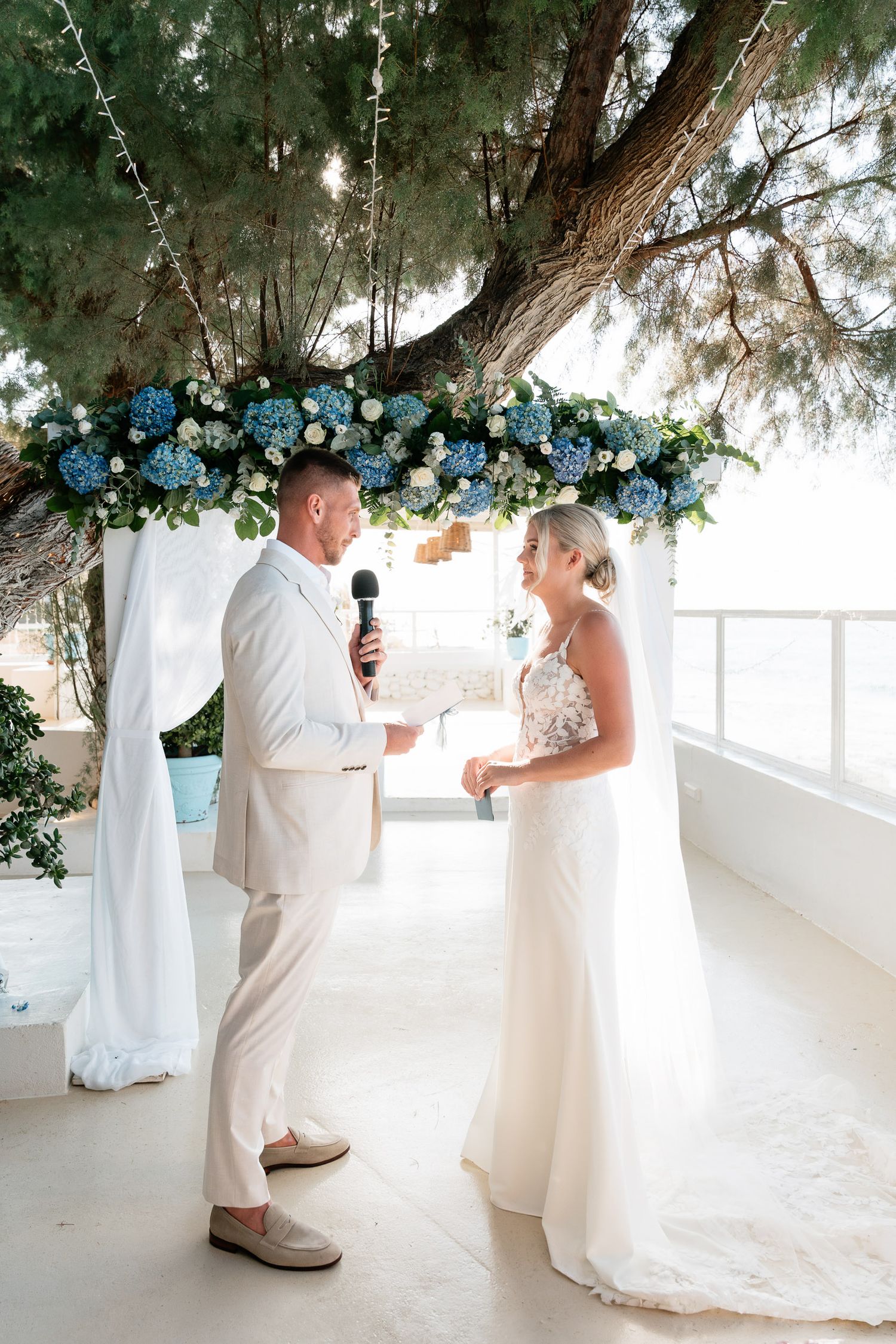 A romantic wedding ceremony sequence showing a couple in white attire exchanging vows under floral decorations by the sea.