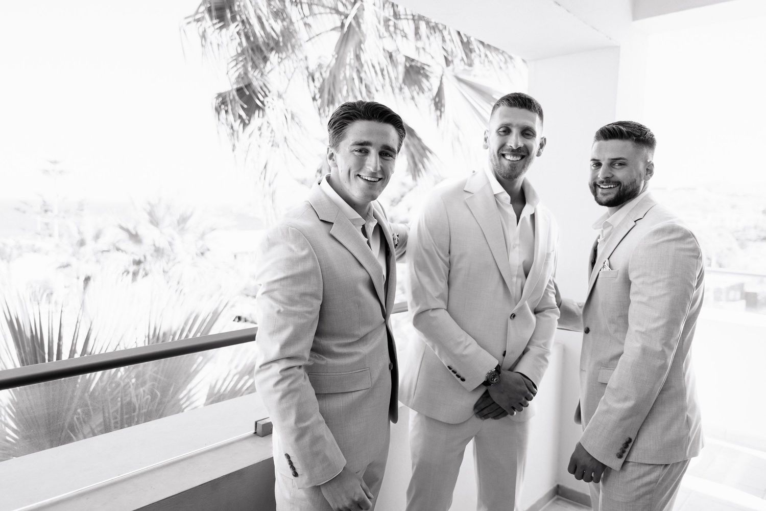 Groomsmen in light gray suits share a laugh while getting ready for a wedding celebration.