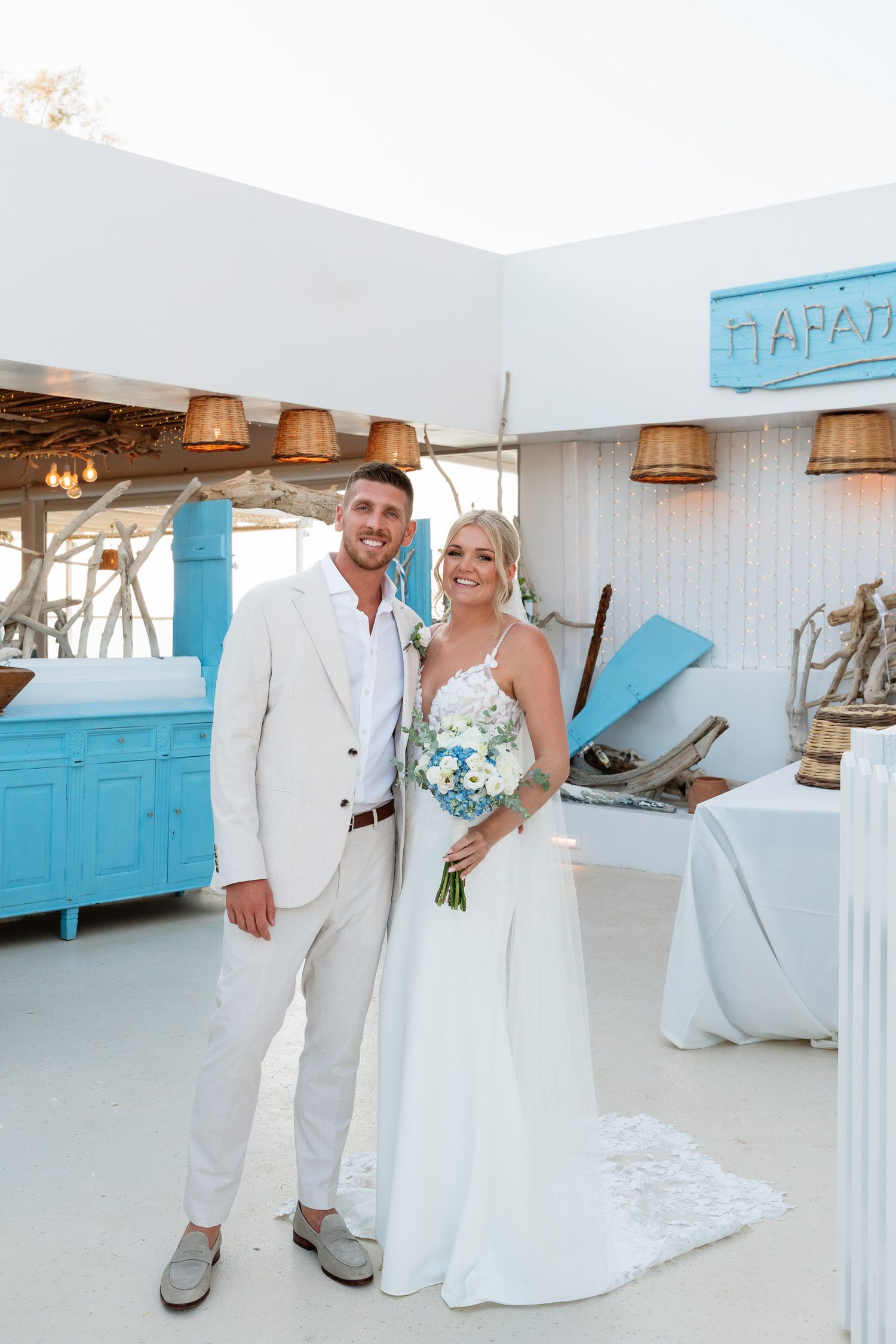 A couple poses at a beachy wedding venue with white walls, turquoise accents and woven basket light fixtures.