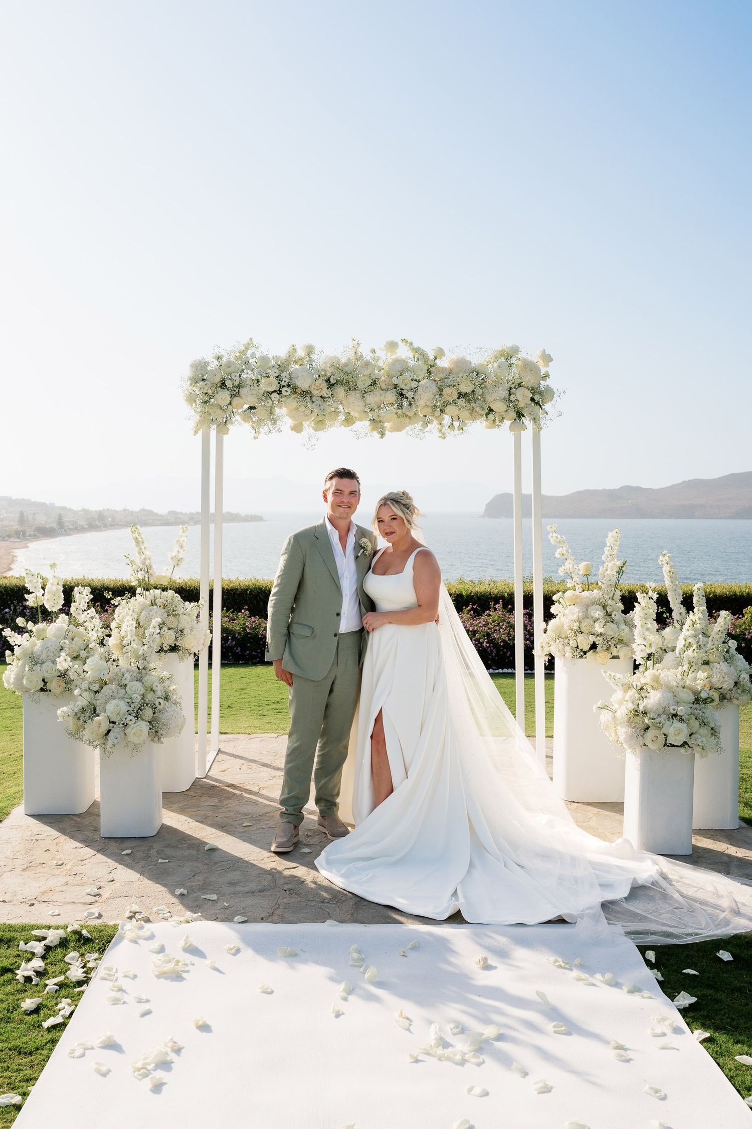 Elegant outdoor wedding ceremony setup with white floral arch and aisle decorations against a scenic mountain backdrop.
