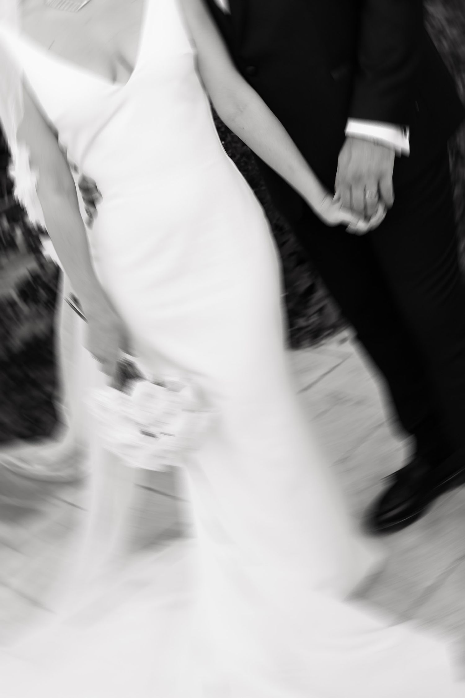 Motion blurred black and white image of people dancing with focus on feet and flowing white fabric.