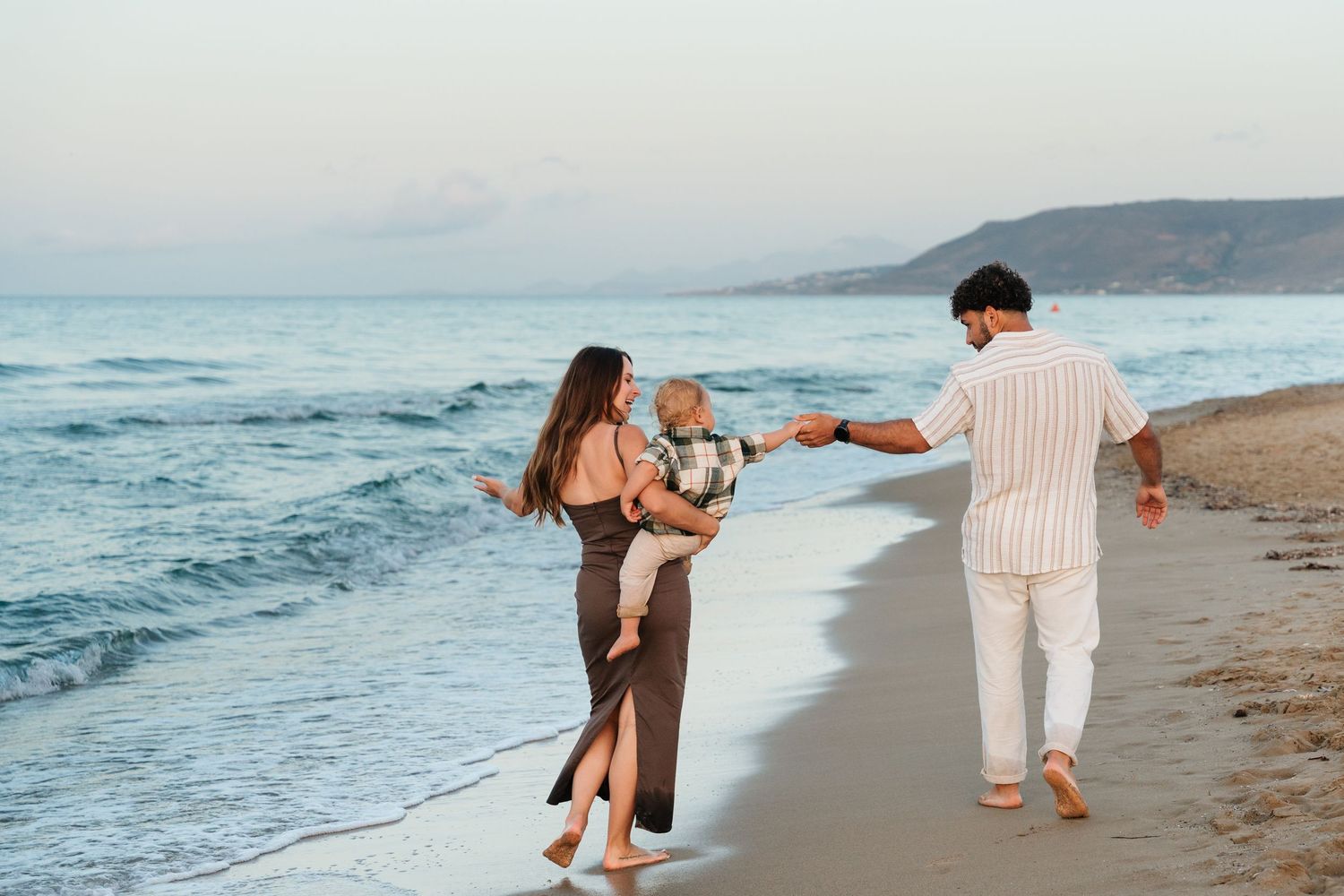 A couple in casual attire walks playfully along the beach at sunset with ocean waves in the background.
